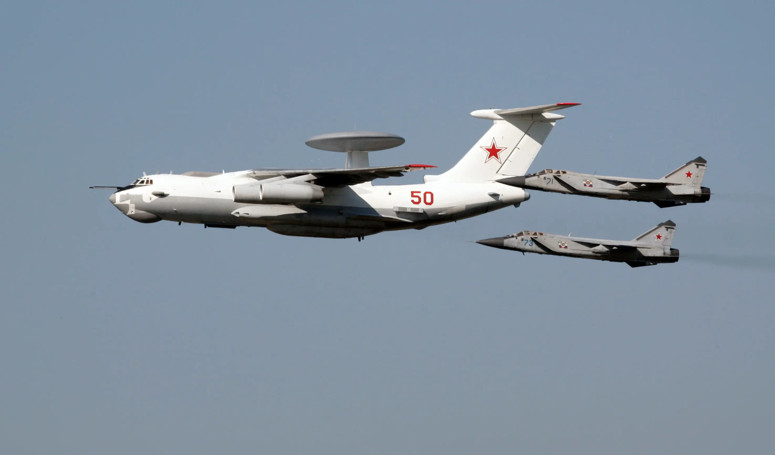 A large white aircraft in a grey sky with two smaller grey jets flying behind it