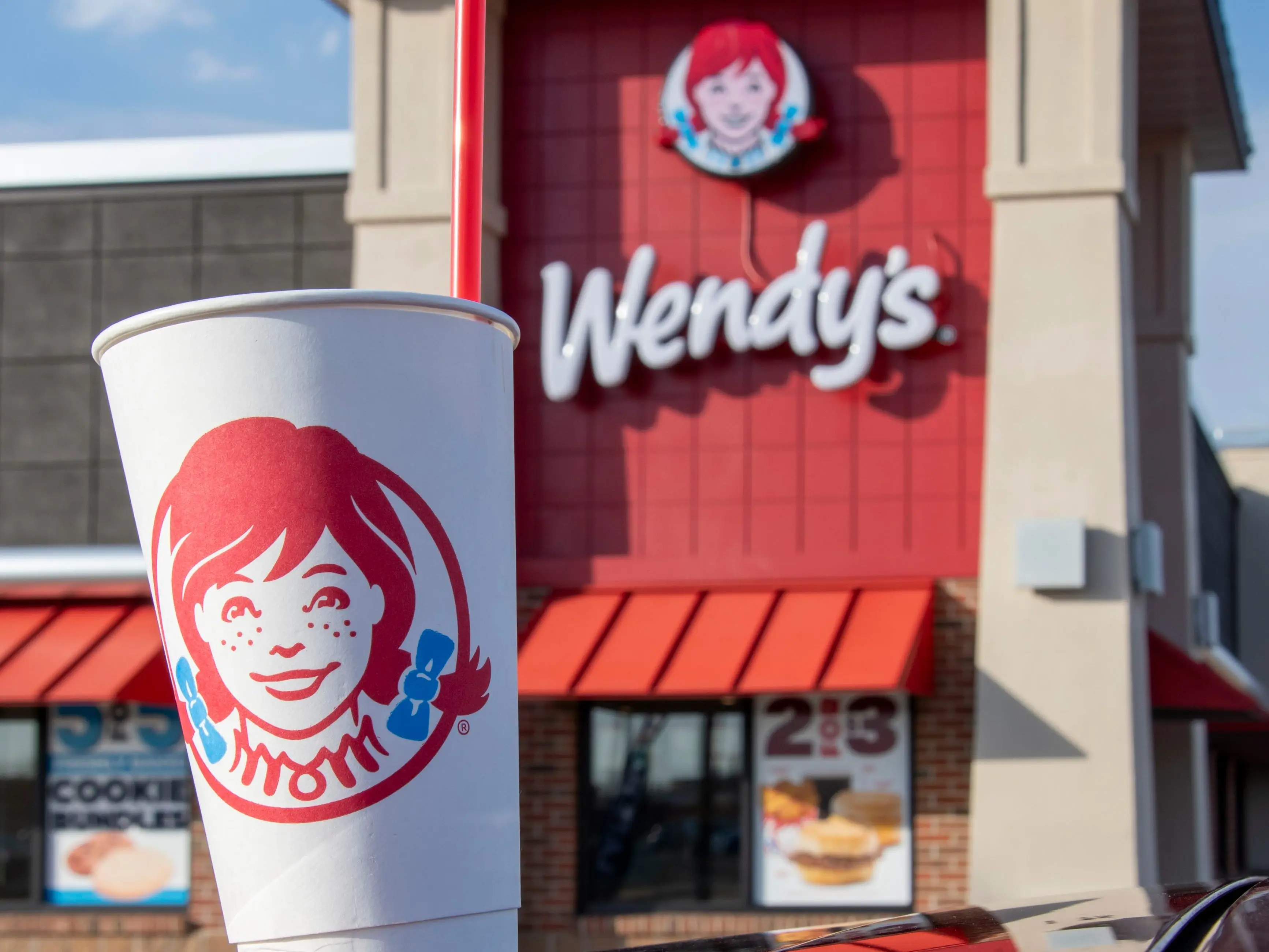 Wendy's fast food chain exterior of building with logo and drink cup in foreground.