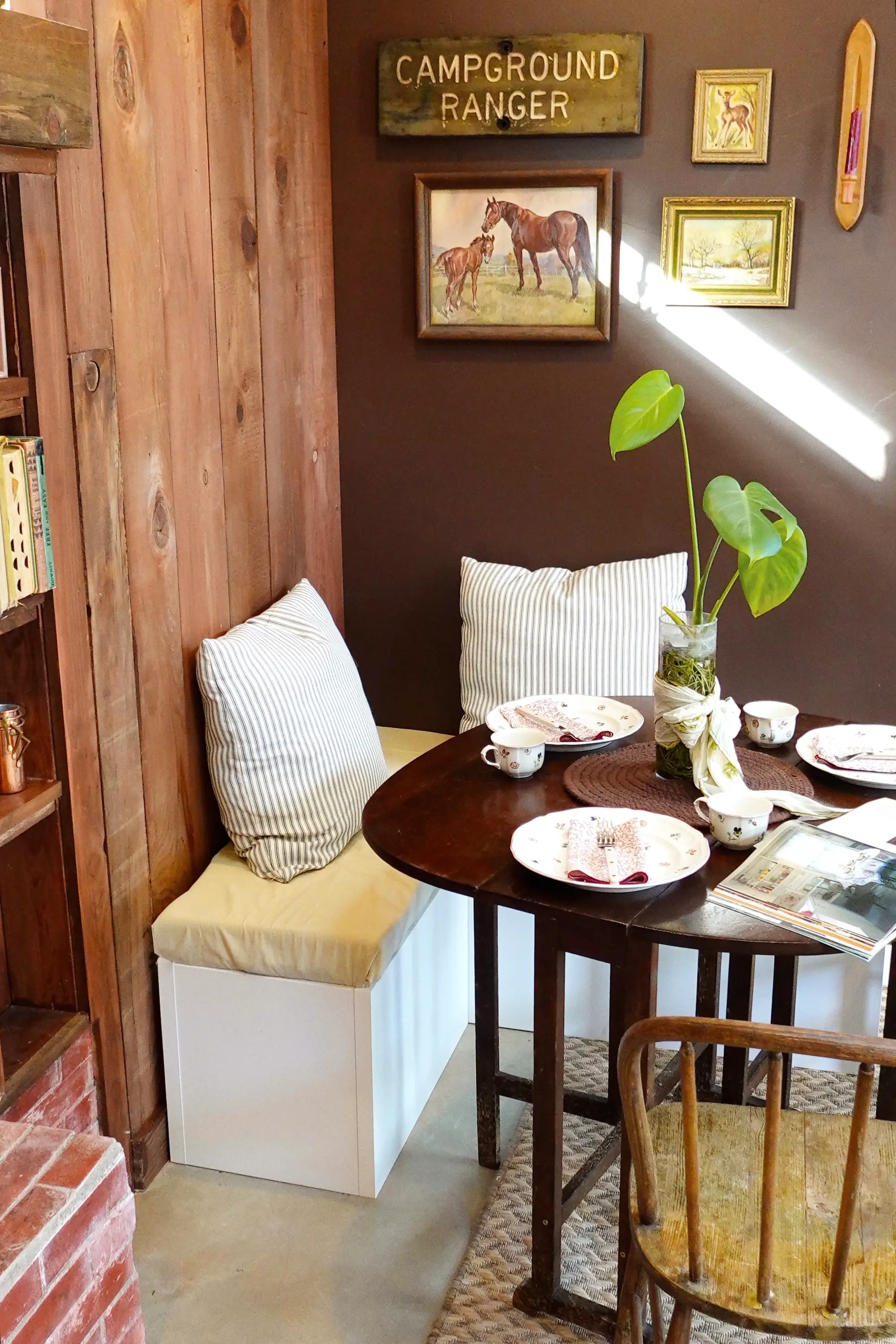 A table with benched seating and an array of paintings hanging on the wall around it.