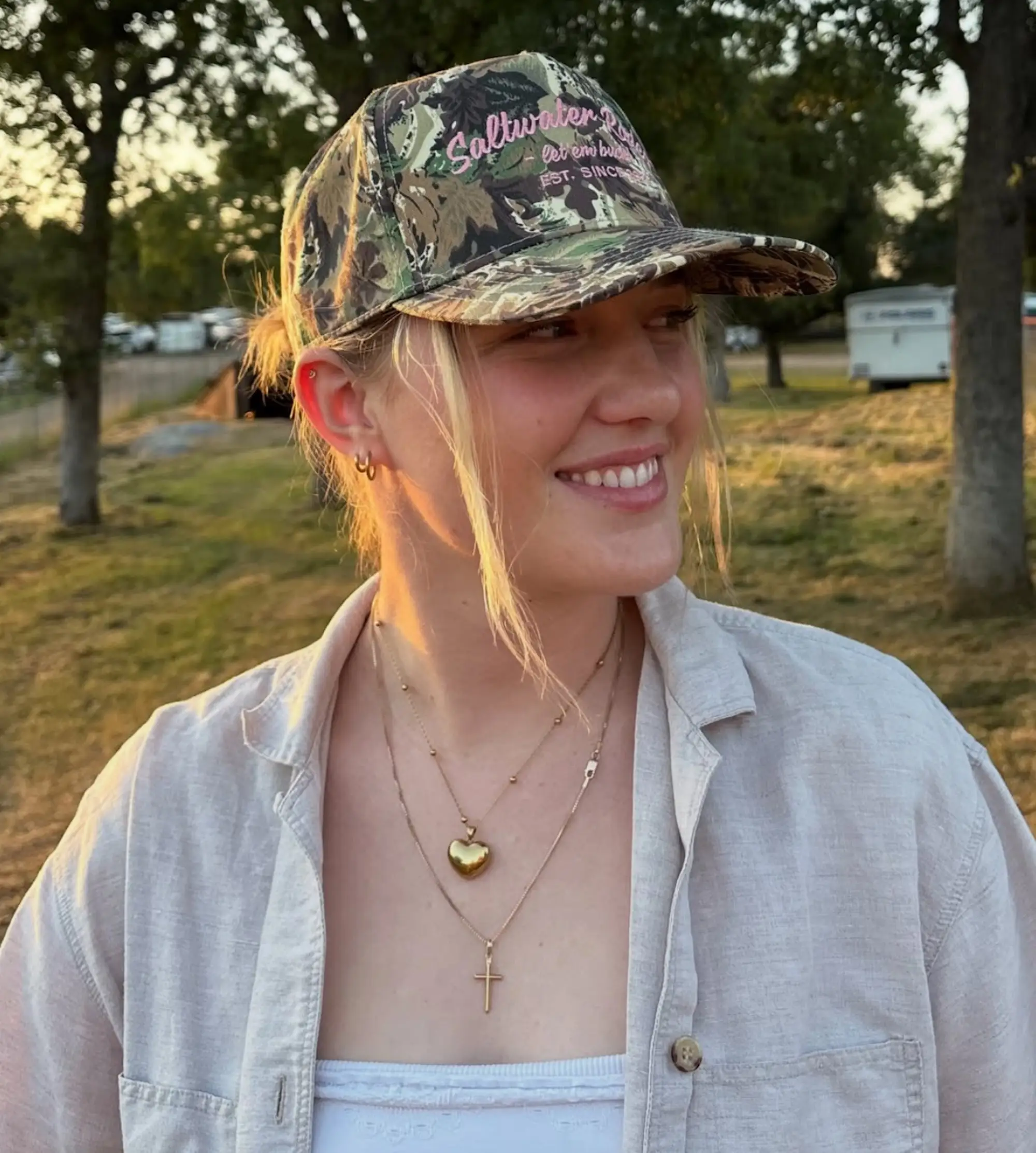 A woman in a camo hat smiles at something off to the right of the camera.