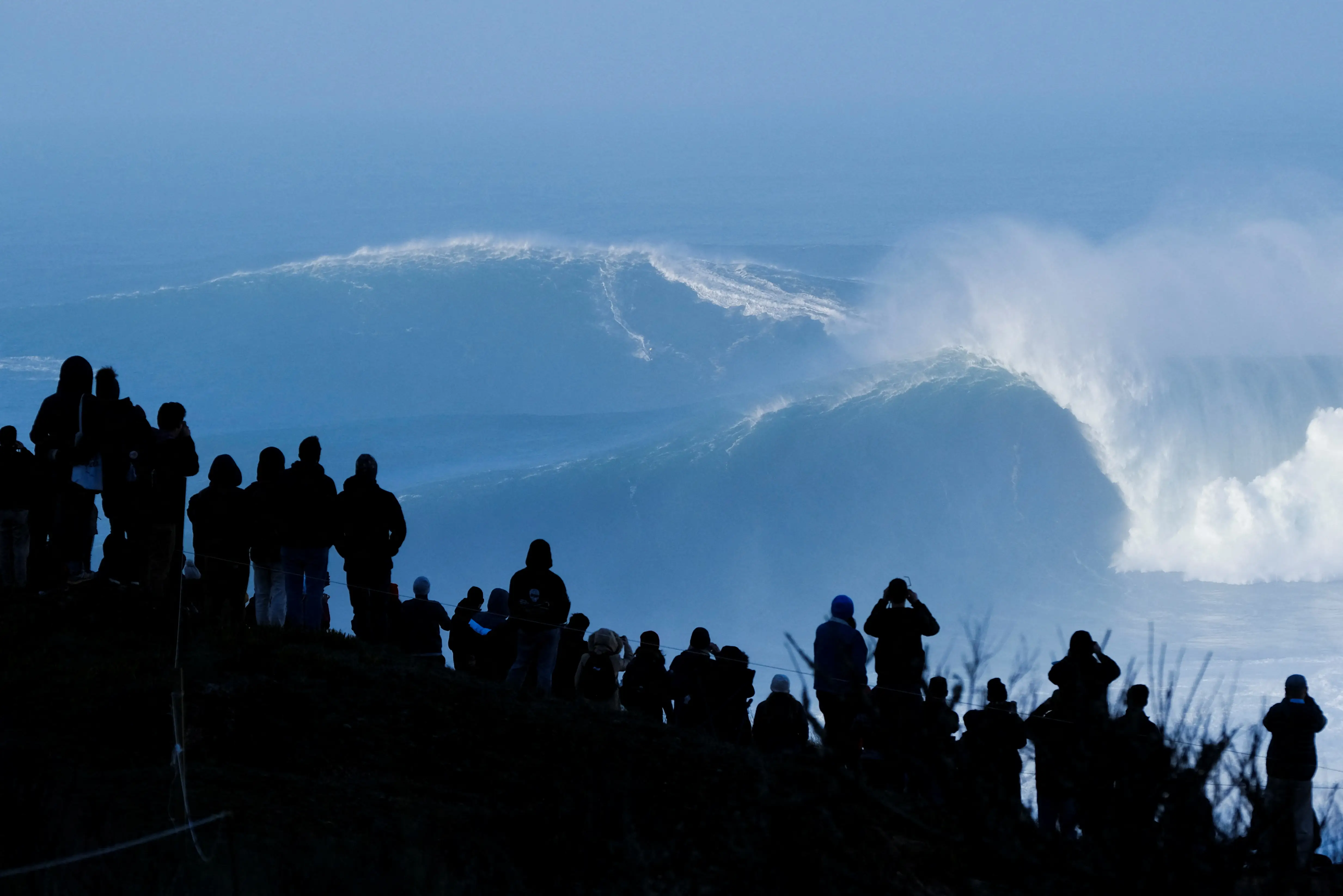 People watch a surfer riding a wave in Praia do Norte, Nazare, Portugal