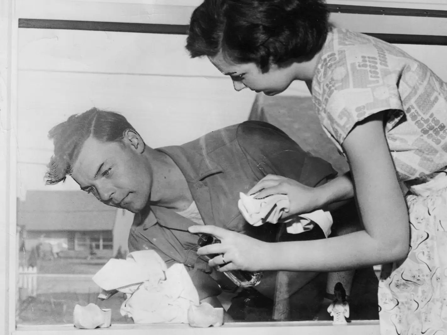 A man and a woman clean opposite sides of a window.