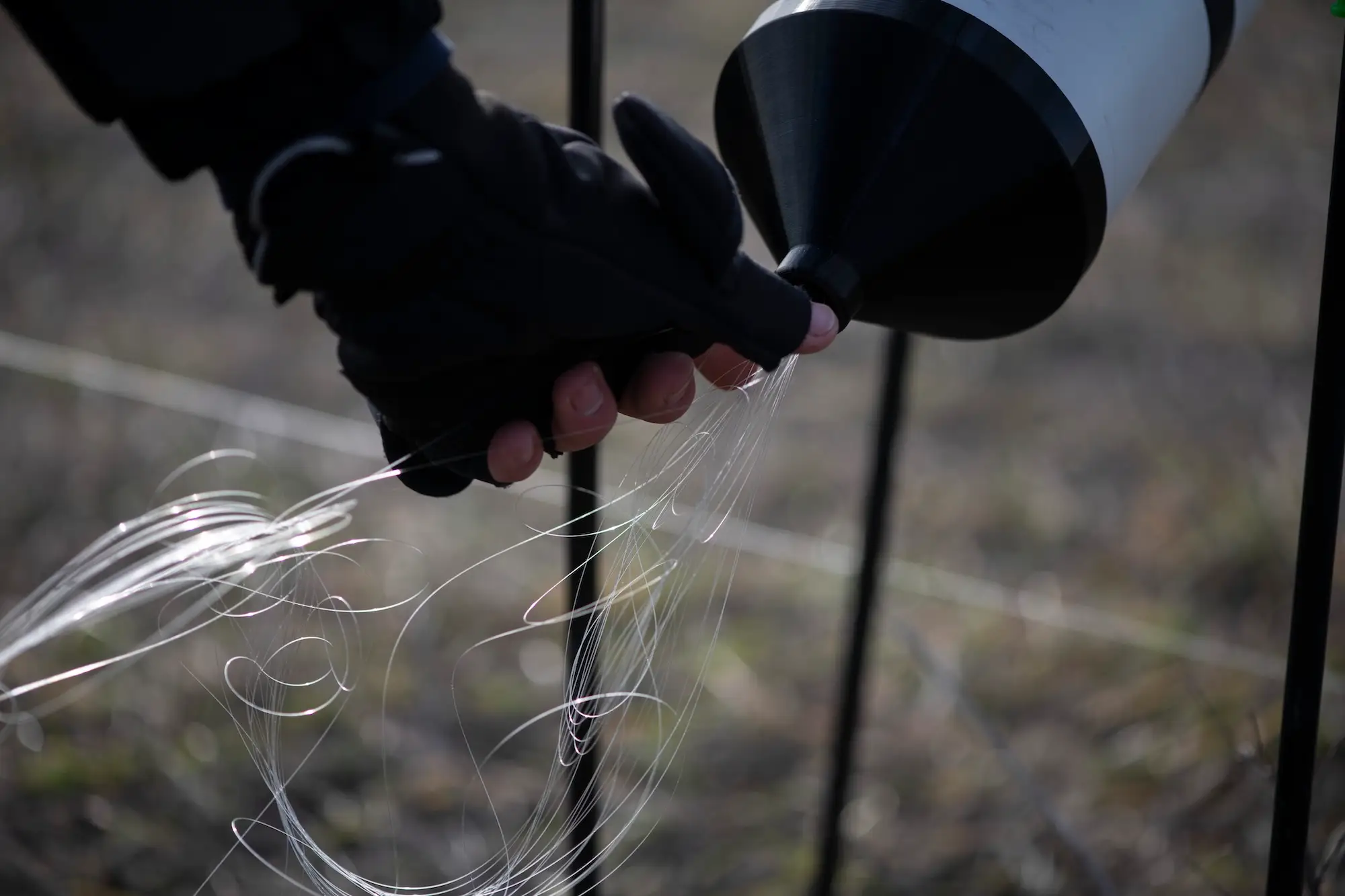 Thin pale wires come out of a black and white cylinder with a gloved hand holding them