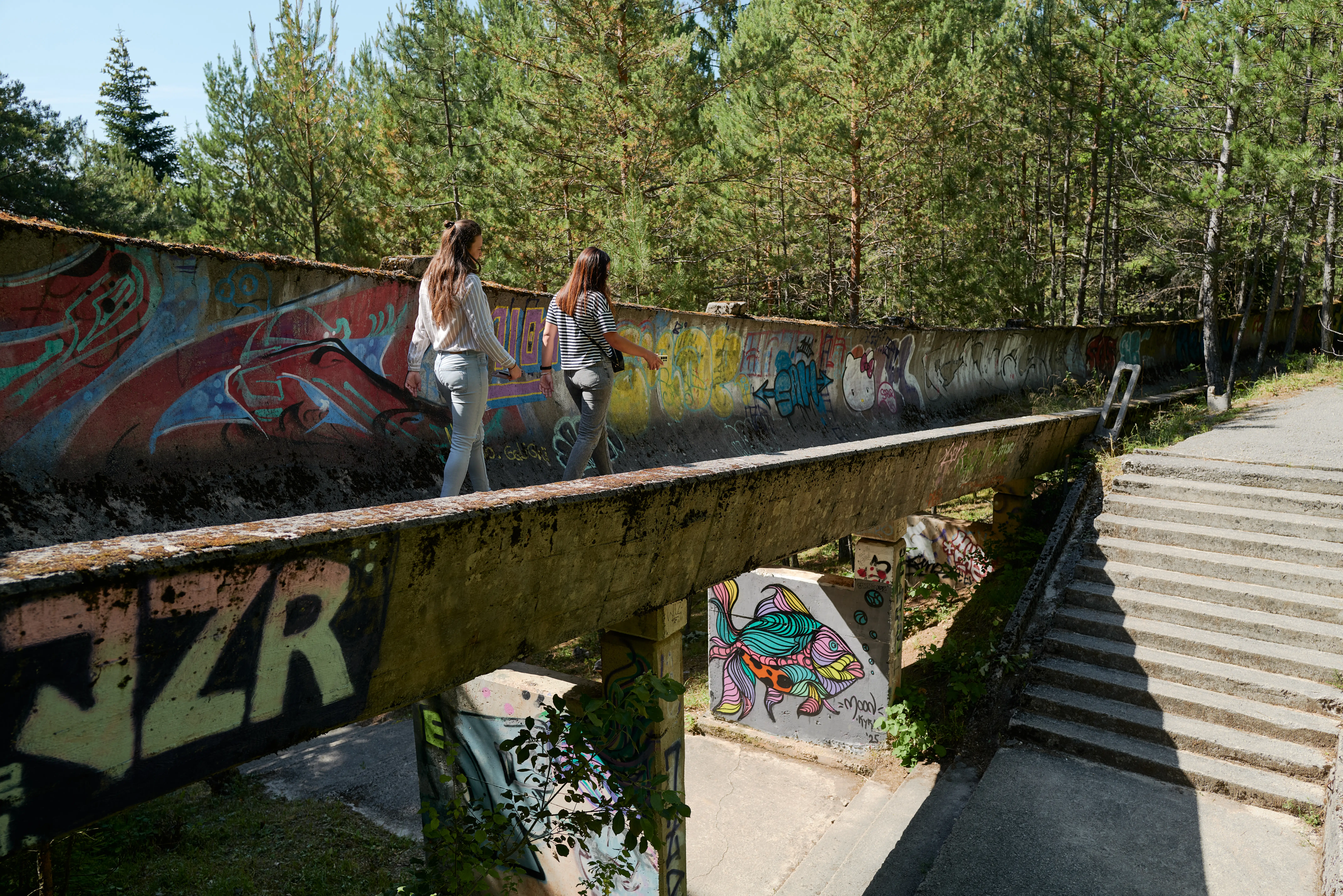 People walk along the Sarajevo bobsleigh track on Mount Trebevi, built for the 1984 Winter Olympics and later repurposed by Bosnian Serb forces as an artillery position during The 1992-1995 siege of Sarajevo on July 13, 2025 in Sarajevo, Bosnia and Herzegovina. The war ended with the signing of the Dayton Peace Agreement in 1995, which established Bosnia and Herzegovina's current political structure