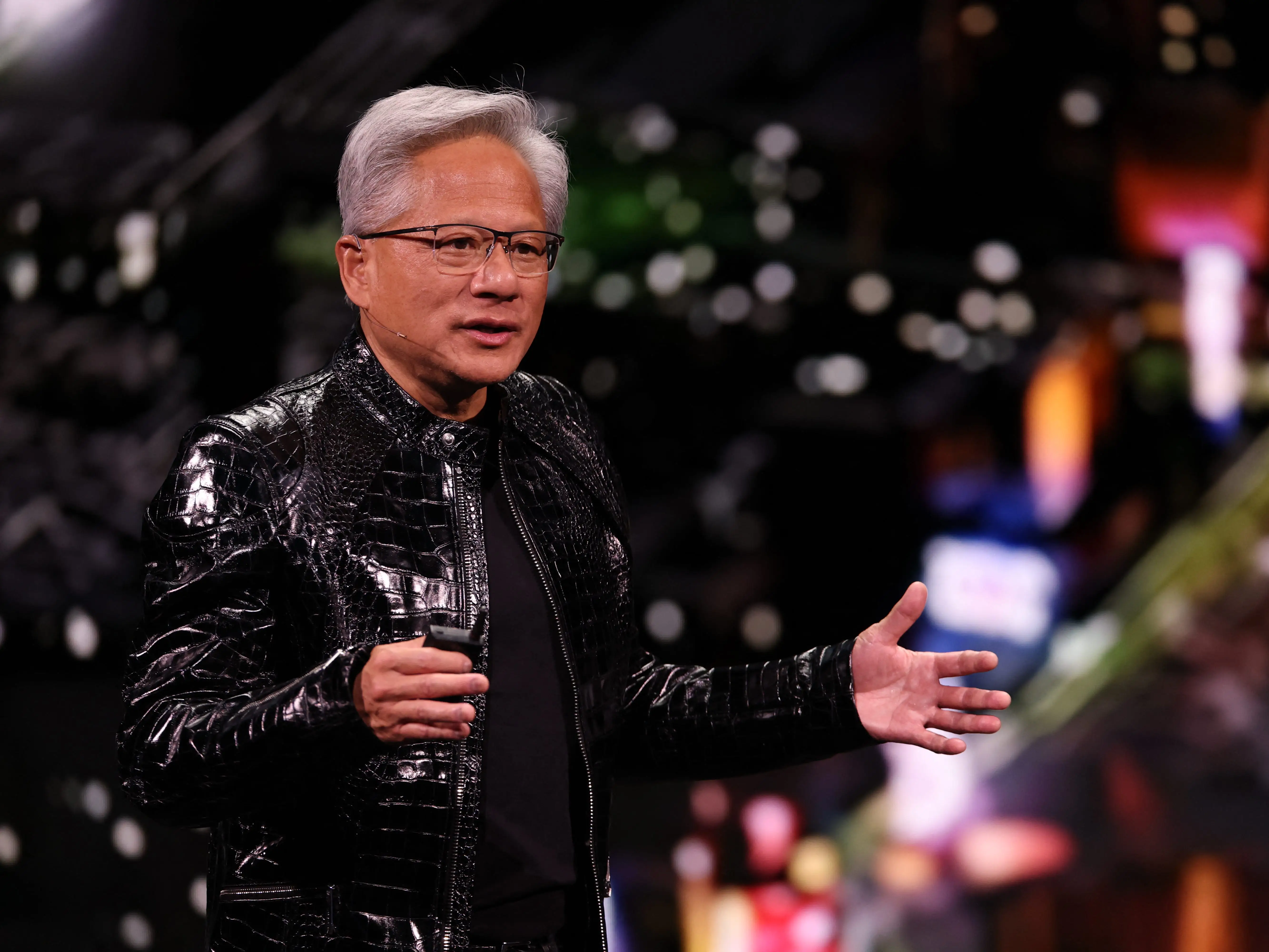 Nvidia cofounder and CEO Jensen Huang onstage in a shiny black jacket with bright lights behind him.