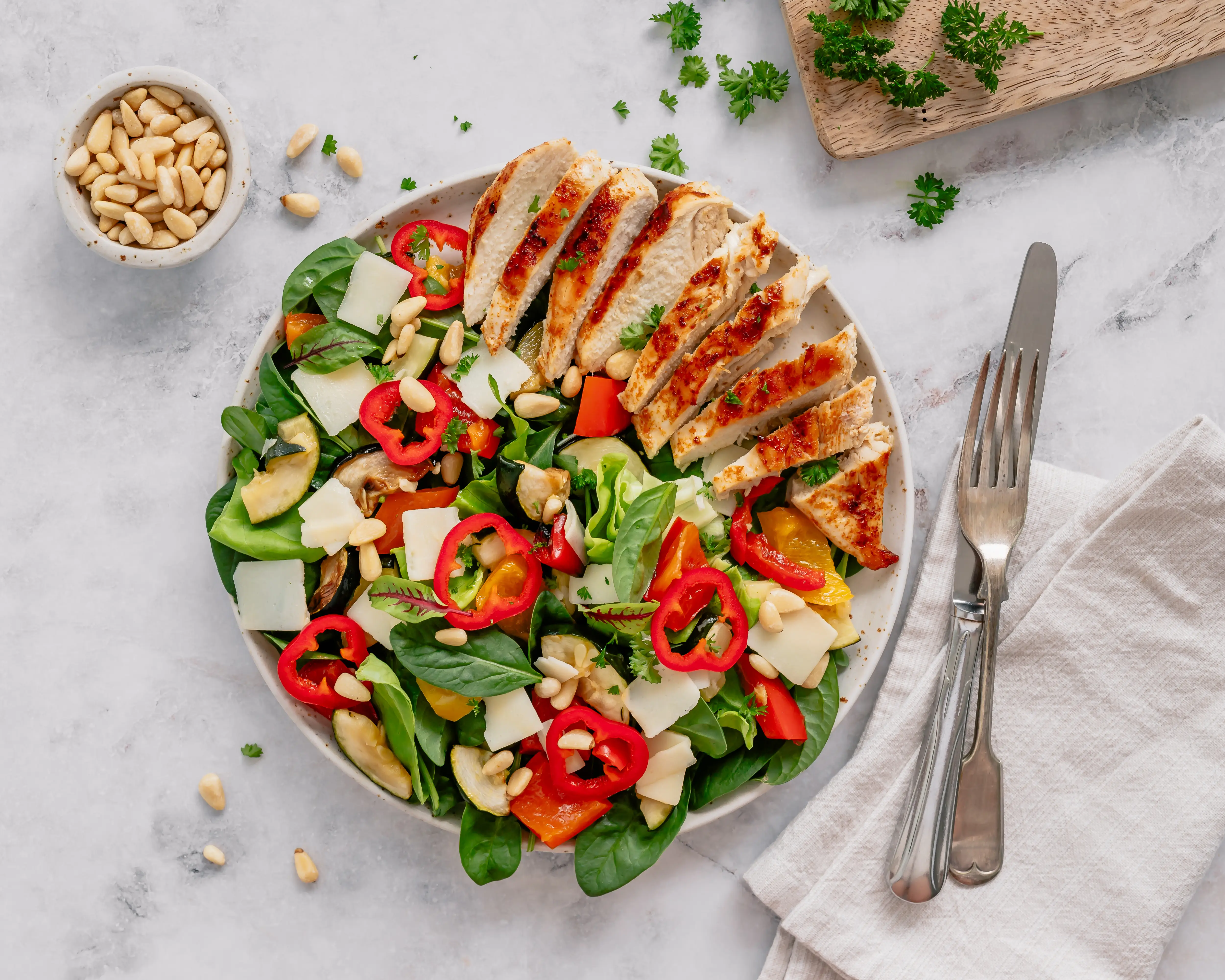 A colorful salad with greens, nuts, peppers, and grilled chicken.