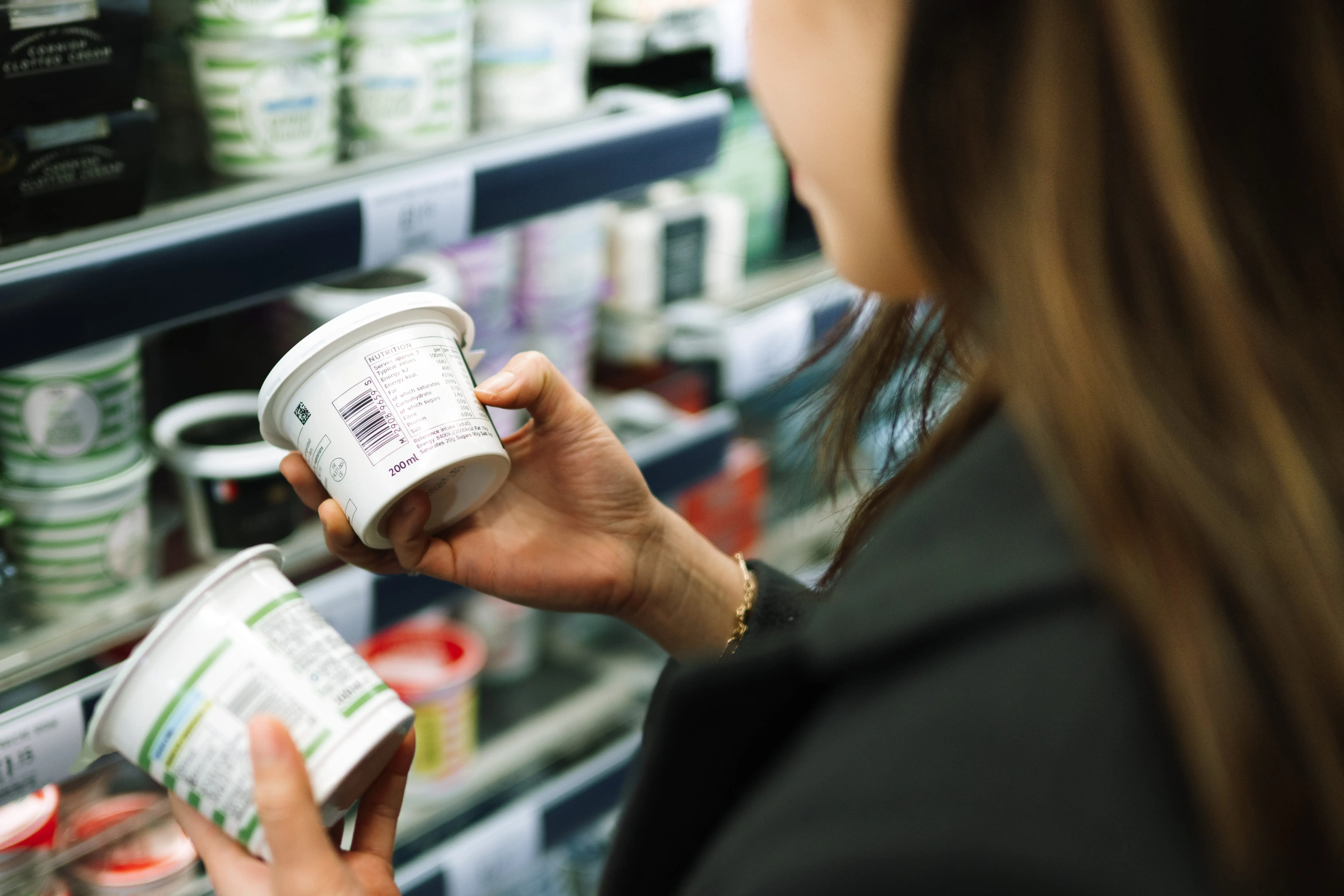 A woman in a grocery store comparing two cartons of dairy