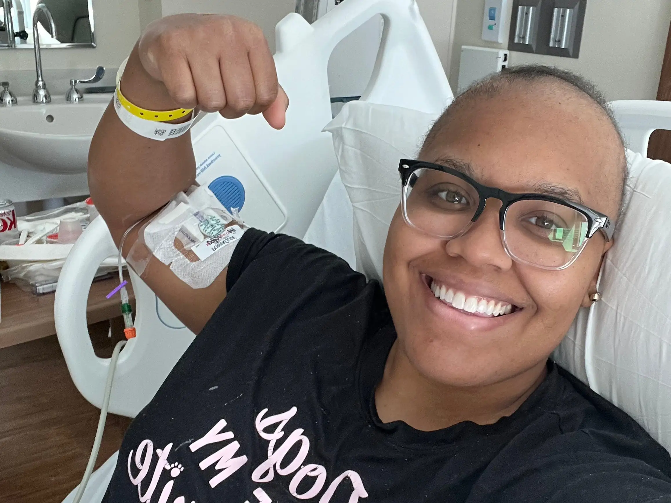 a woman flexing and smiling in a hospital bed during cancer treatment.