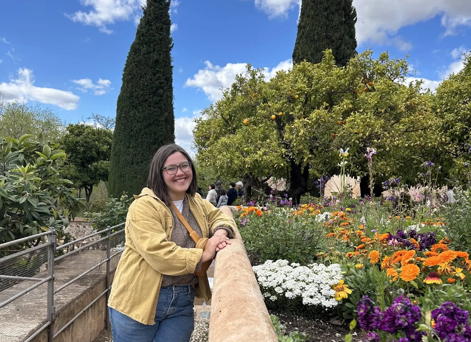 Woman smiling, leaning on stone ledge next to flowers in. Granada