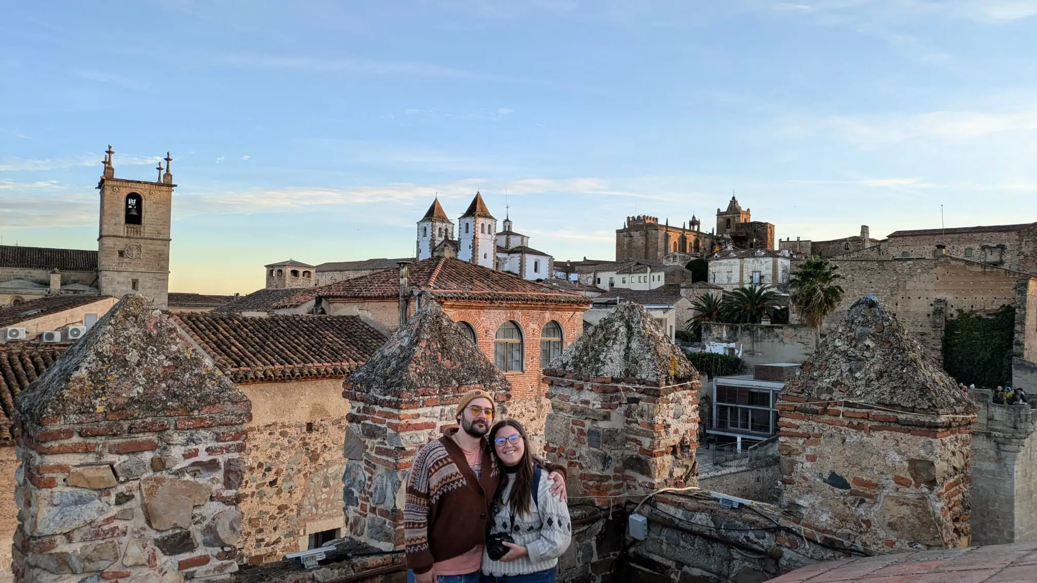 Two people smiling in Caceres with view of building tops behind them