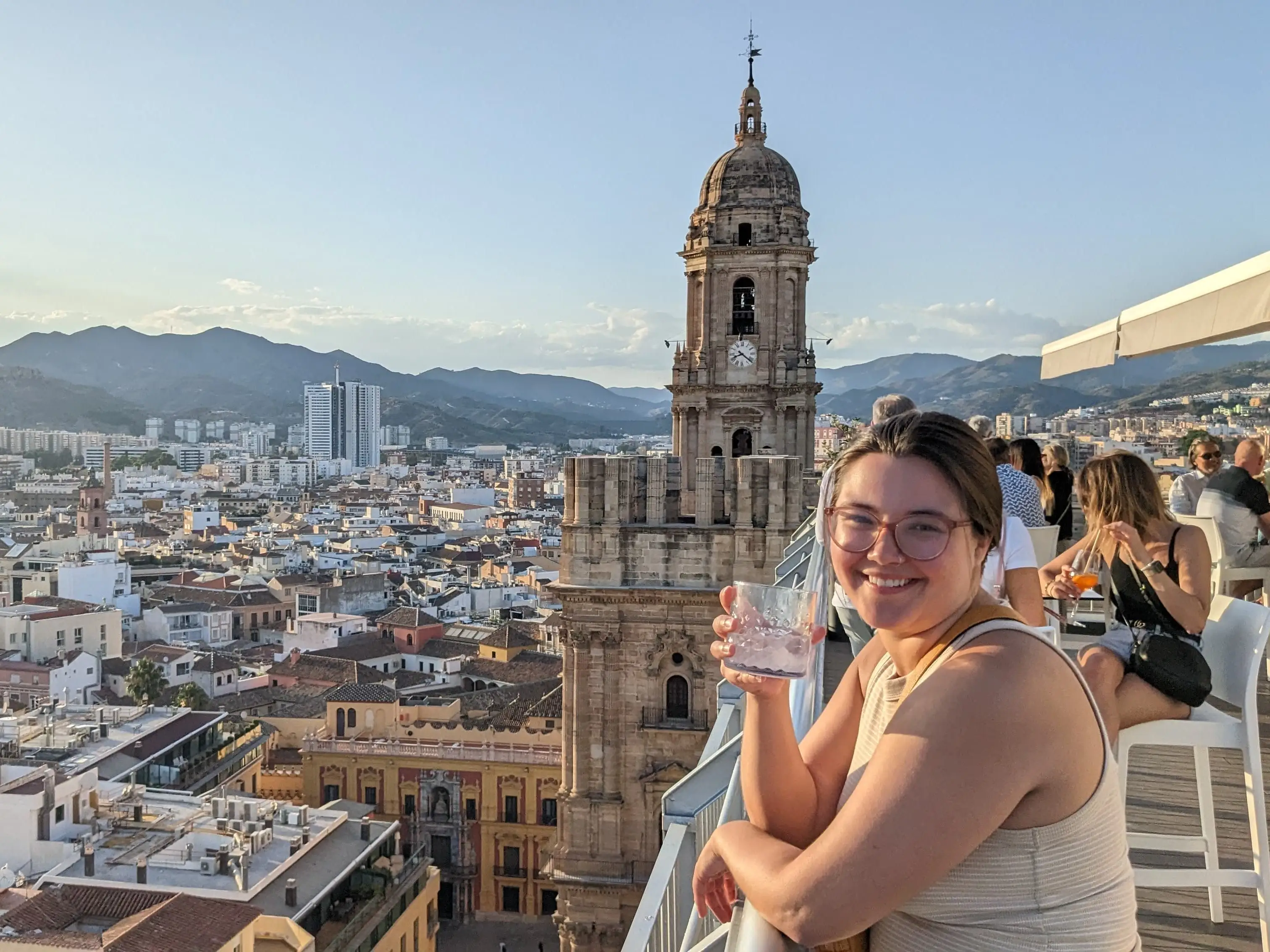 Woman smiling with drink, leaning over balcony in Malaga