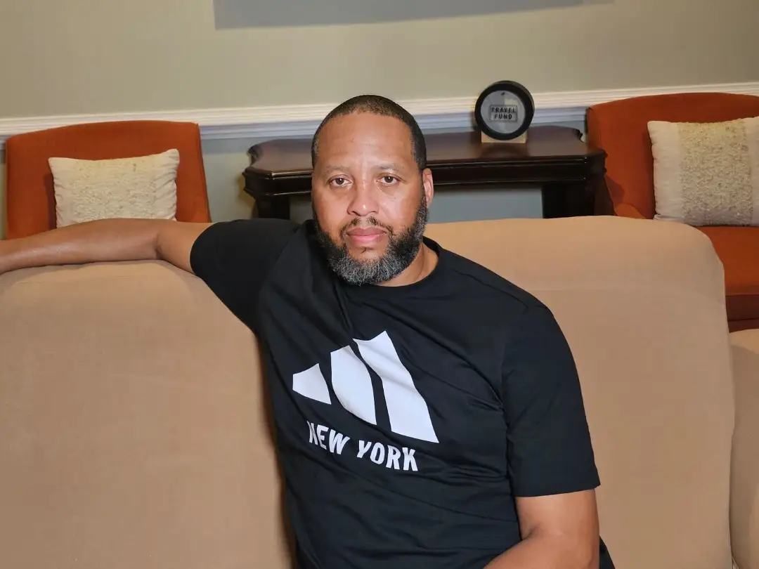 A man in a black T-shirt sitting on a sofa