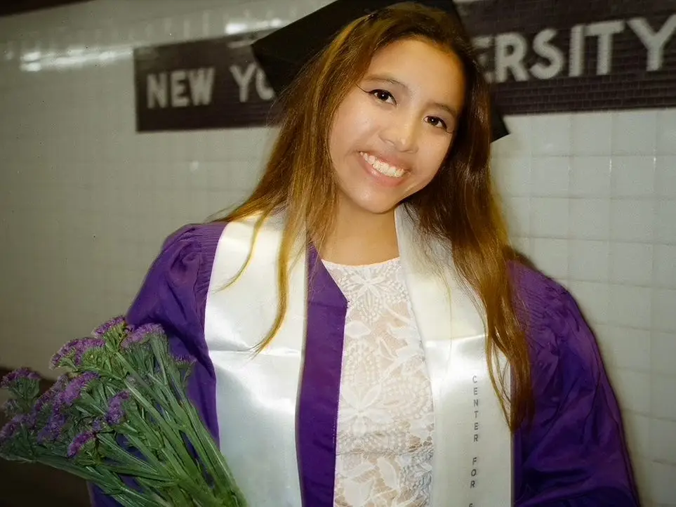 the author in her NYU graduation gown, holding flowers