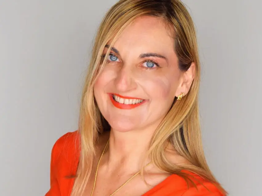 Yesim Saydan headshot. Smiling in a red top with a gray background.