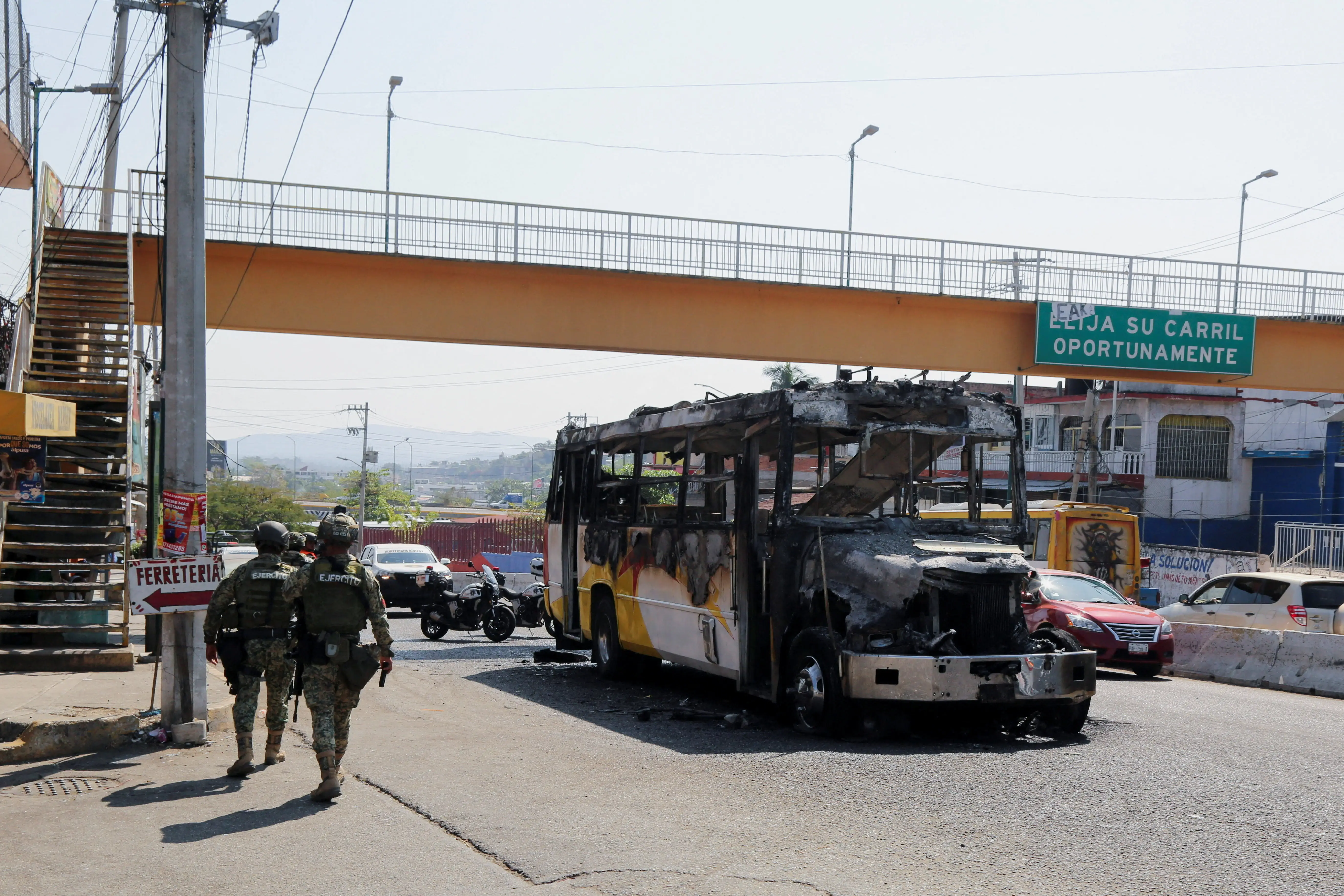 Soldiers walk past a bus torched