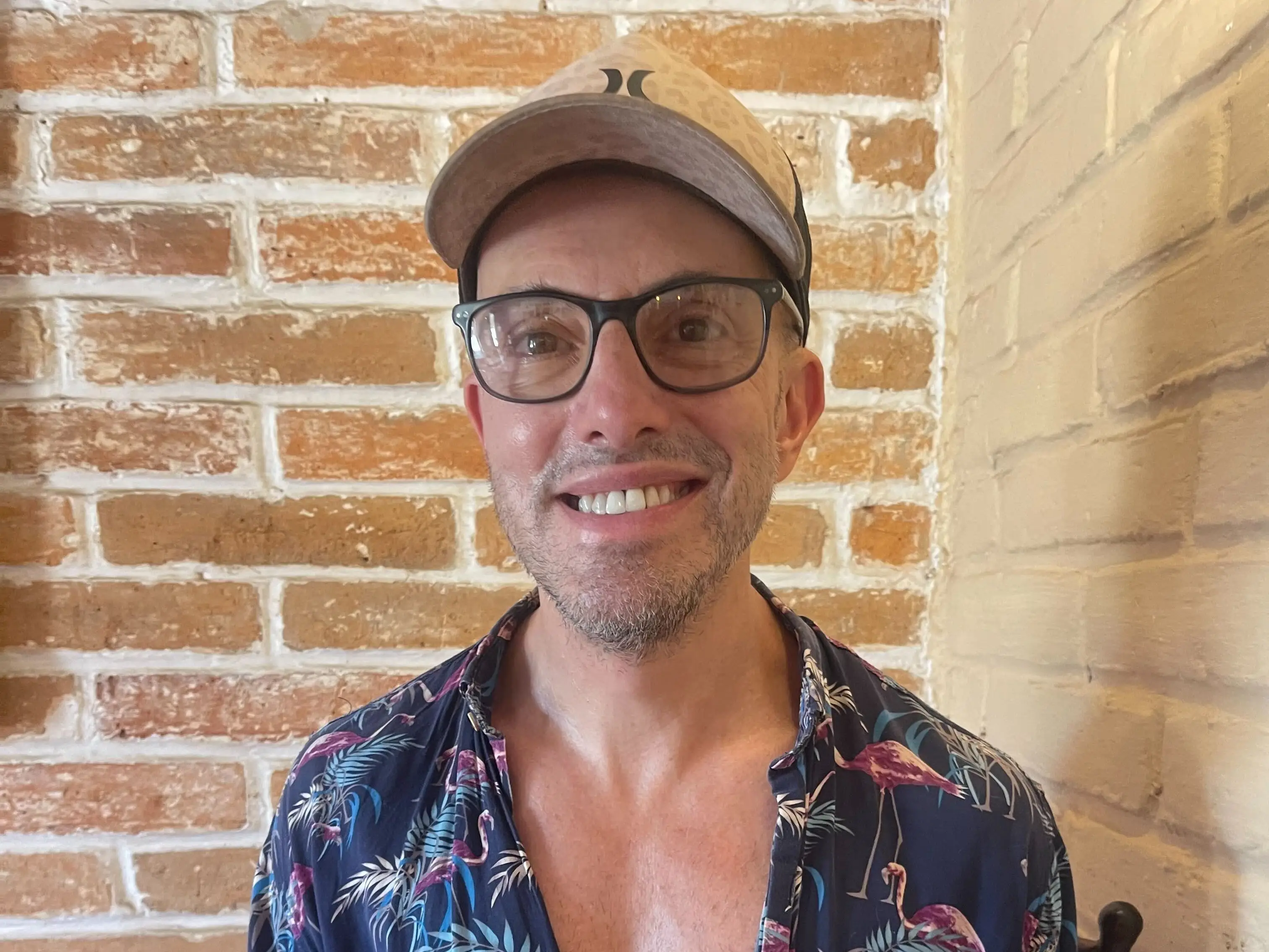 Steven Polito sits in a café holding a mug of coffee against a brick wall.
