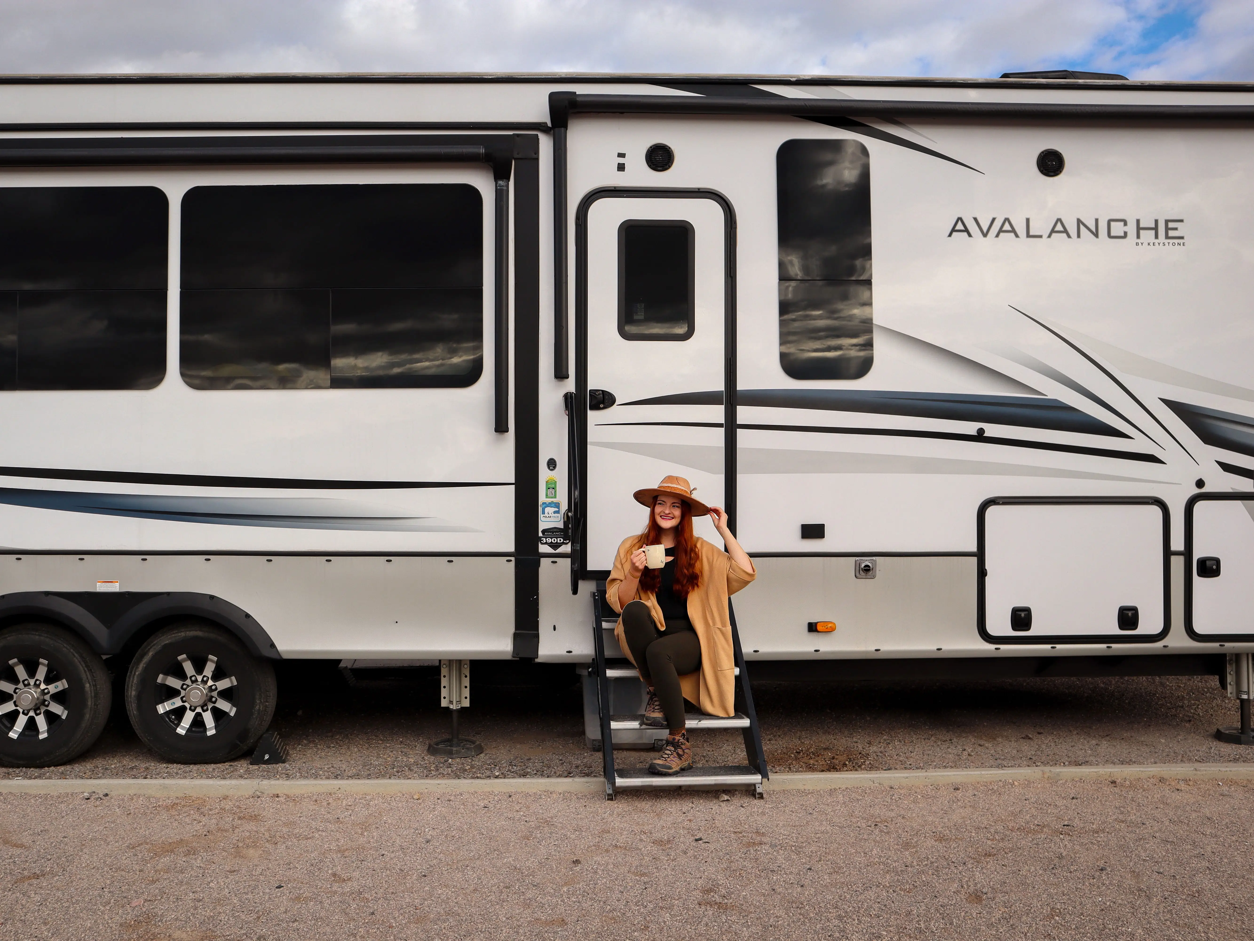Alexandra holds a cup of coffee while sitting on the steps of an RV.