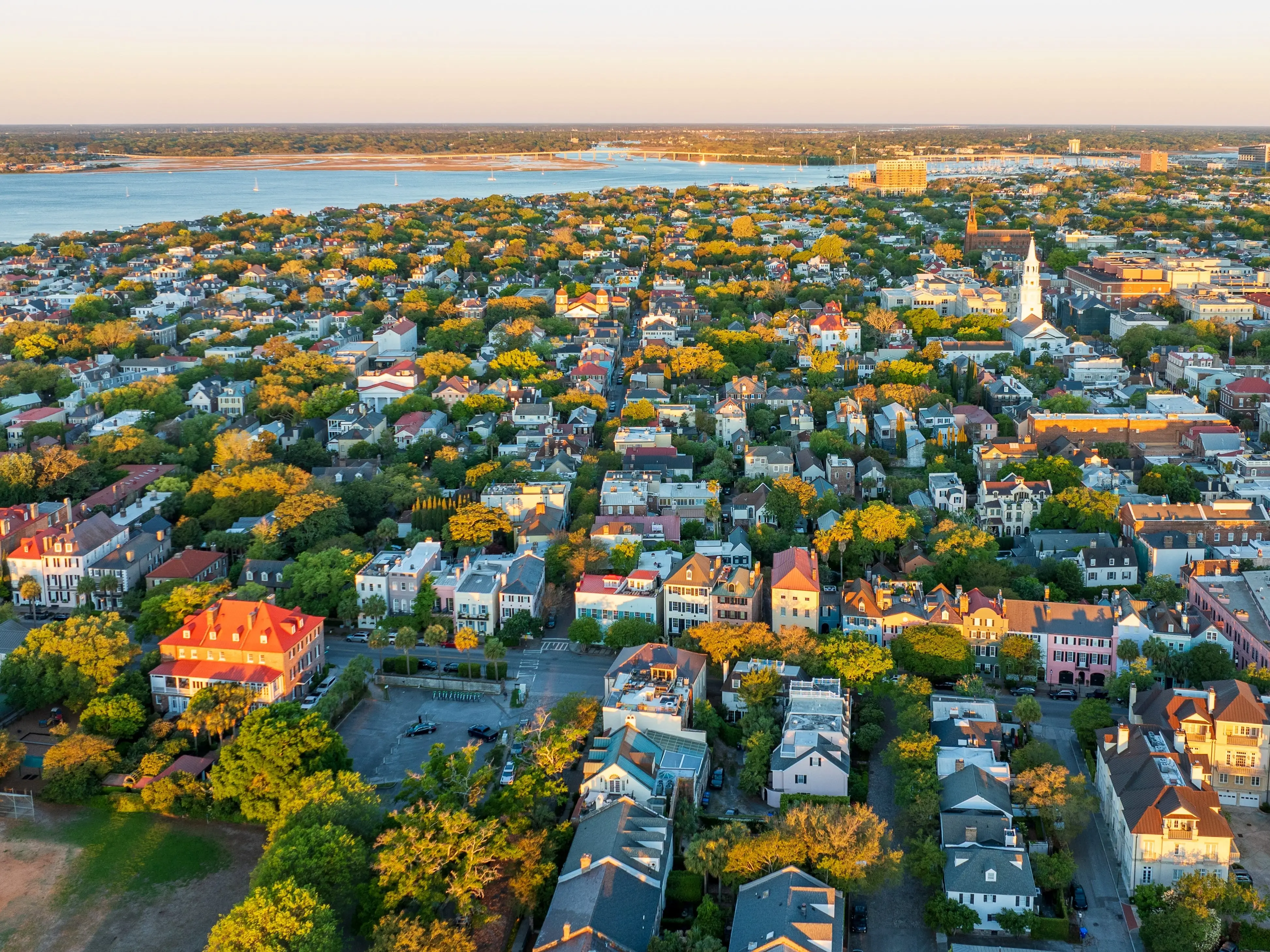 Golden sunrise light bathes downtown Charleston, South Carolina, with historic buildings and streets visible from an aerial view.