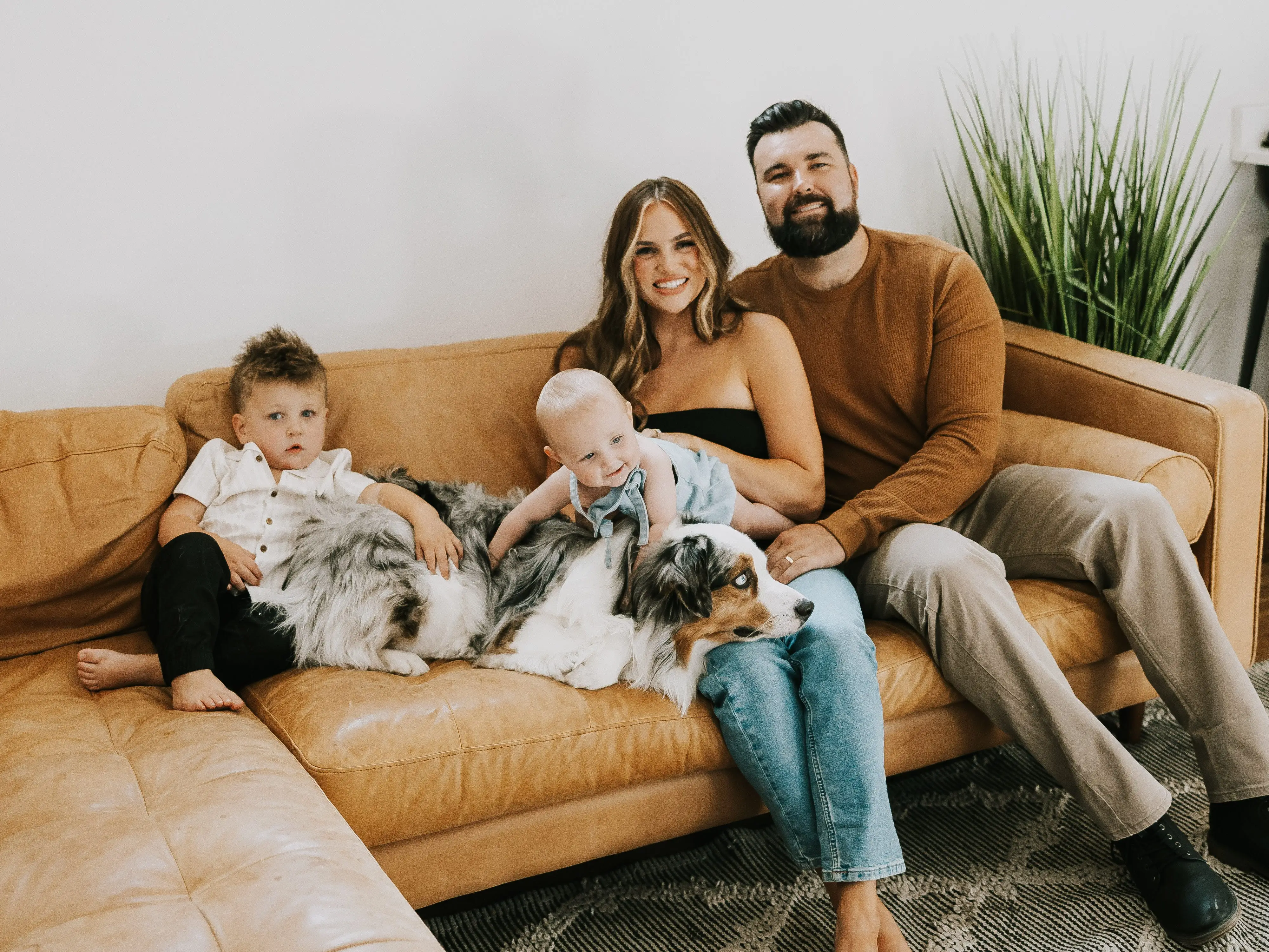 A young damily sits on a couch, a dog on their lap.