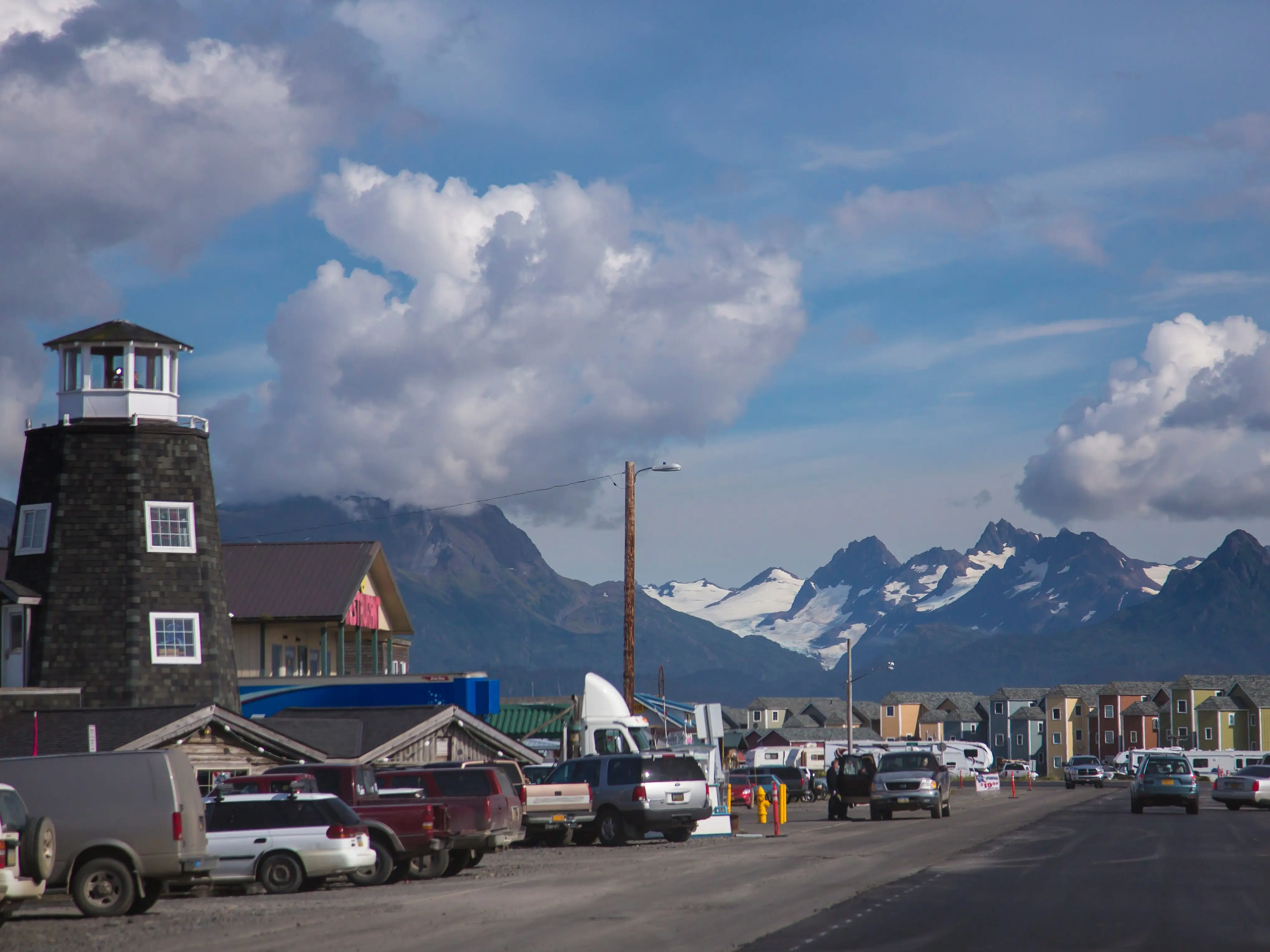 Buildings and cars in a small town with snow-covered mountains in the background.