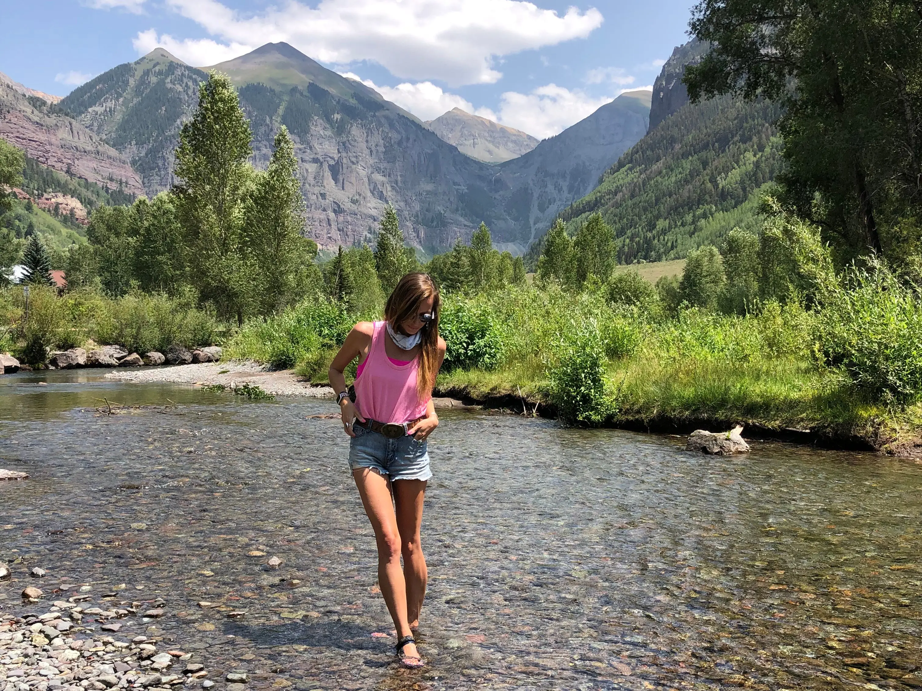 Emily stands in a rocky body of water with trees and mountains in the background.