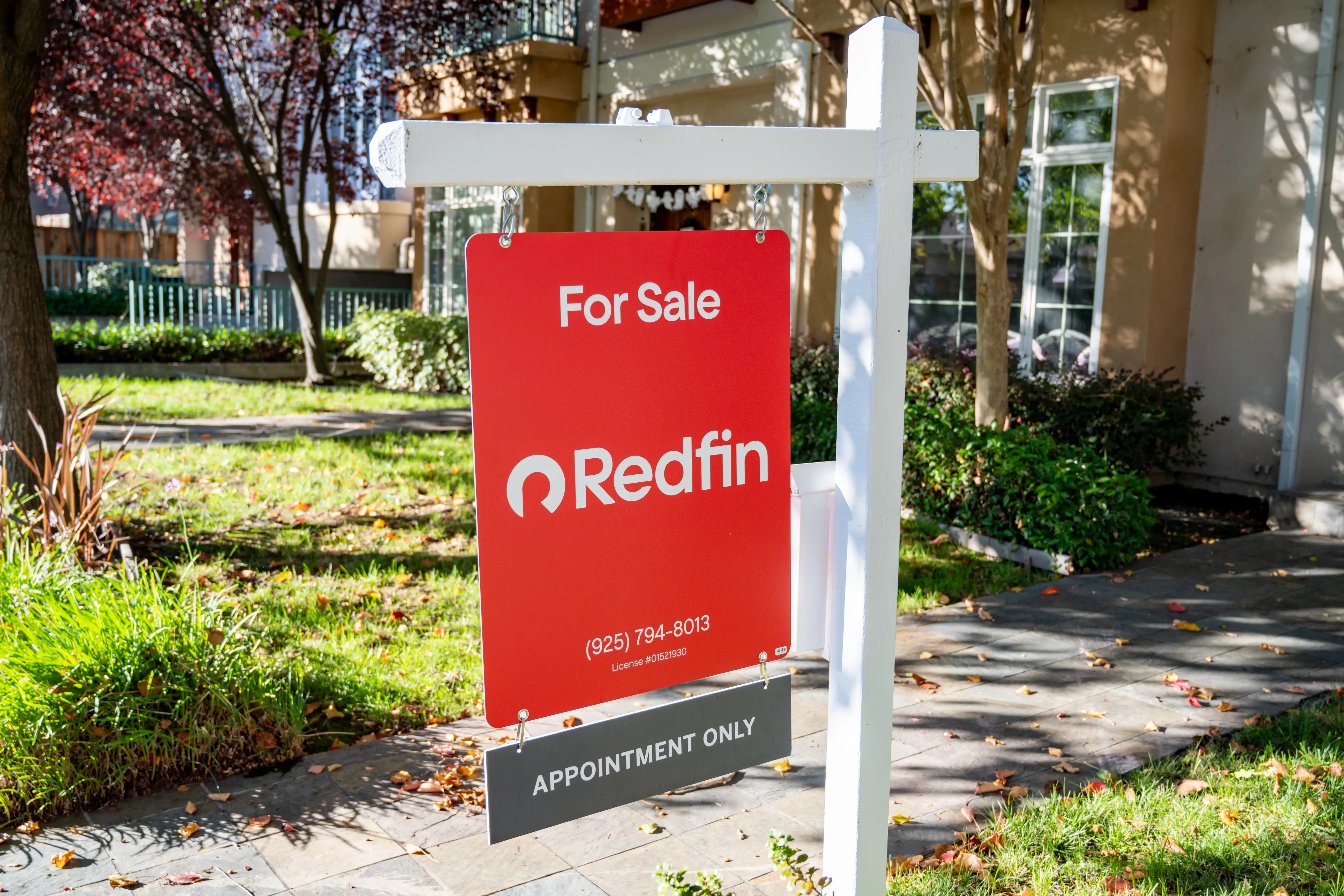 A red for-sale sign from the brokerage firm Redfin in front of a house