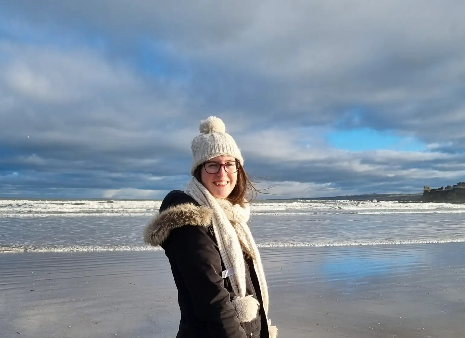 The writer bundled up in a coat and scarf on a beach in St Andrews, Scotland.