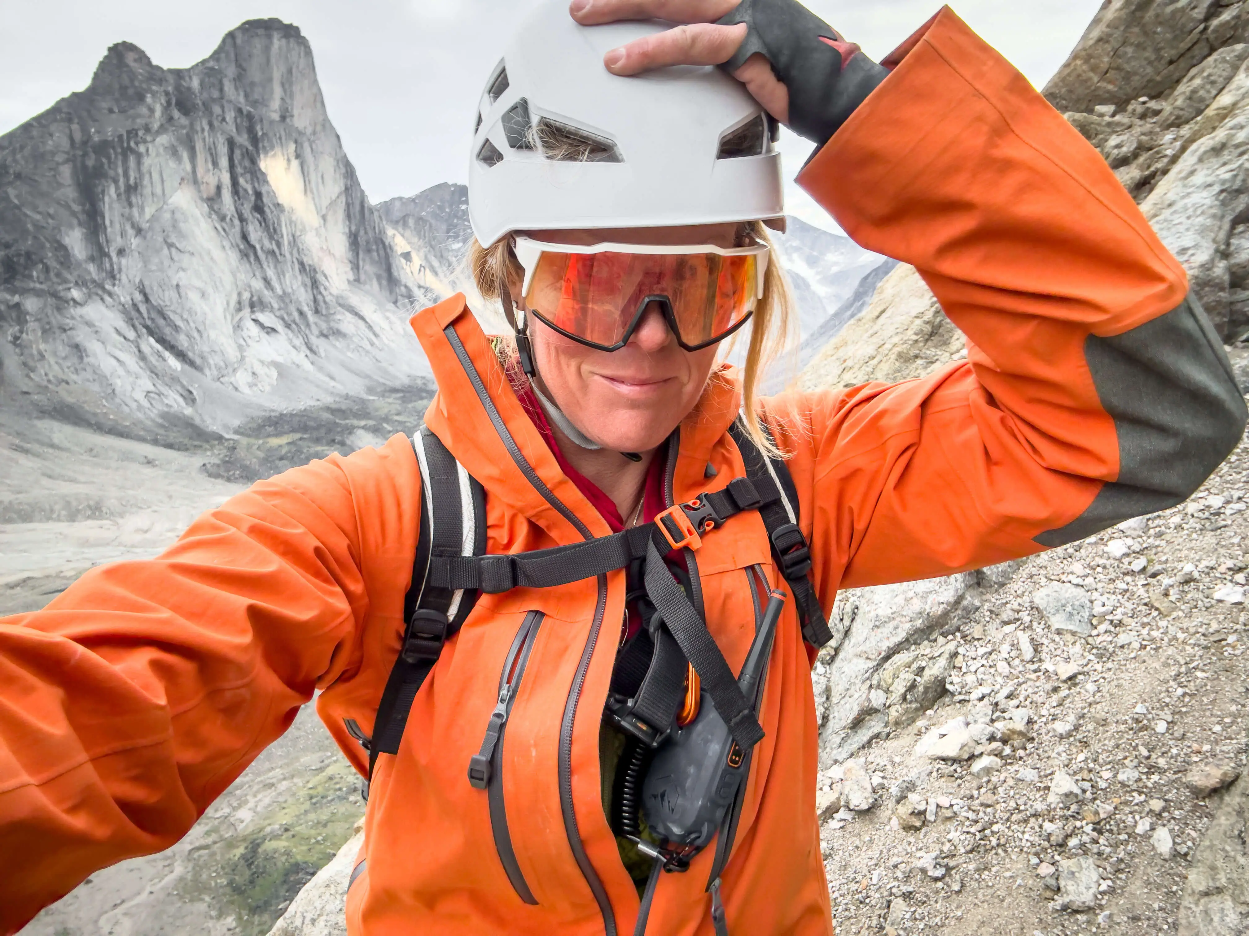 Sunny Stroeer in the mountains wearing an orange jacket, white helmet, and glasses.