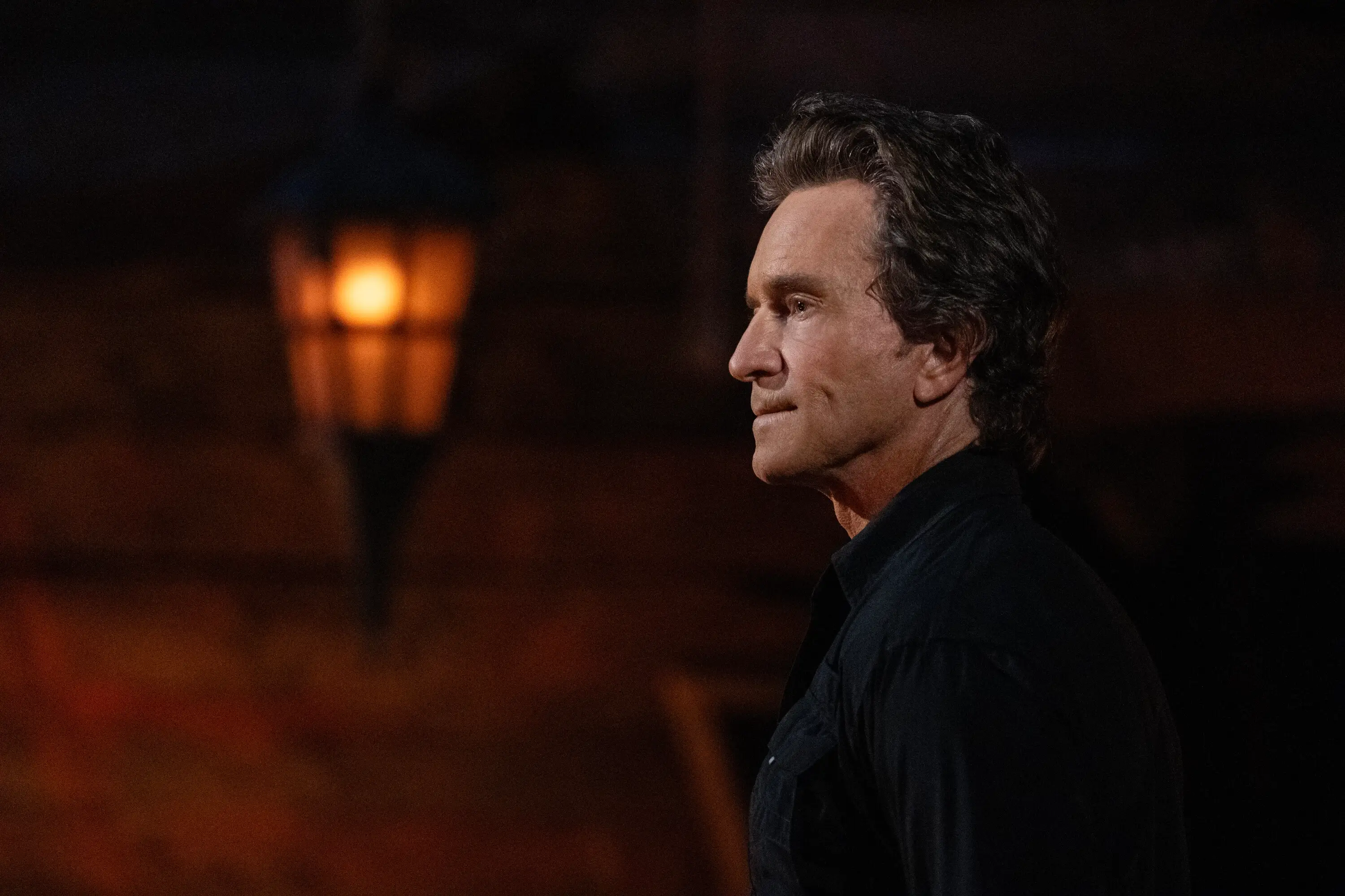 A man stands in side profile in dark light illuminated by a torch.