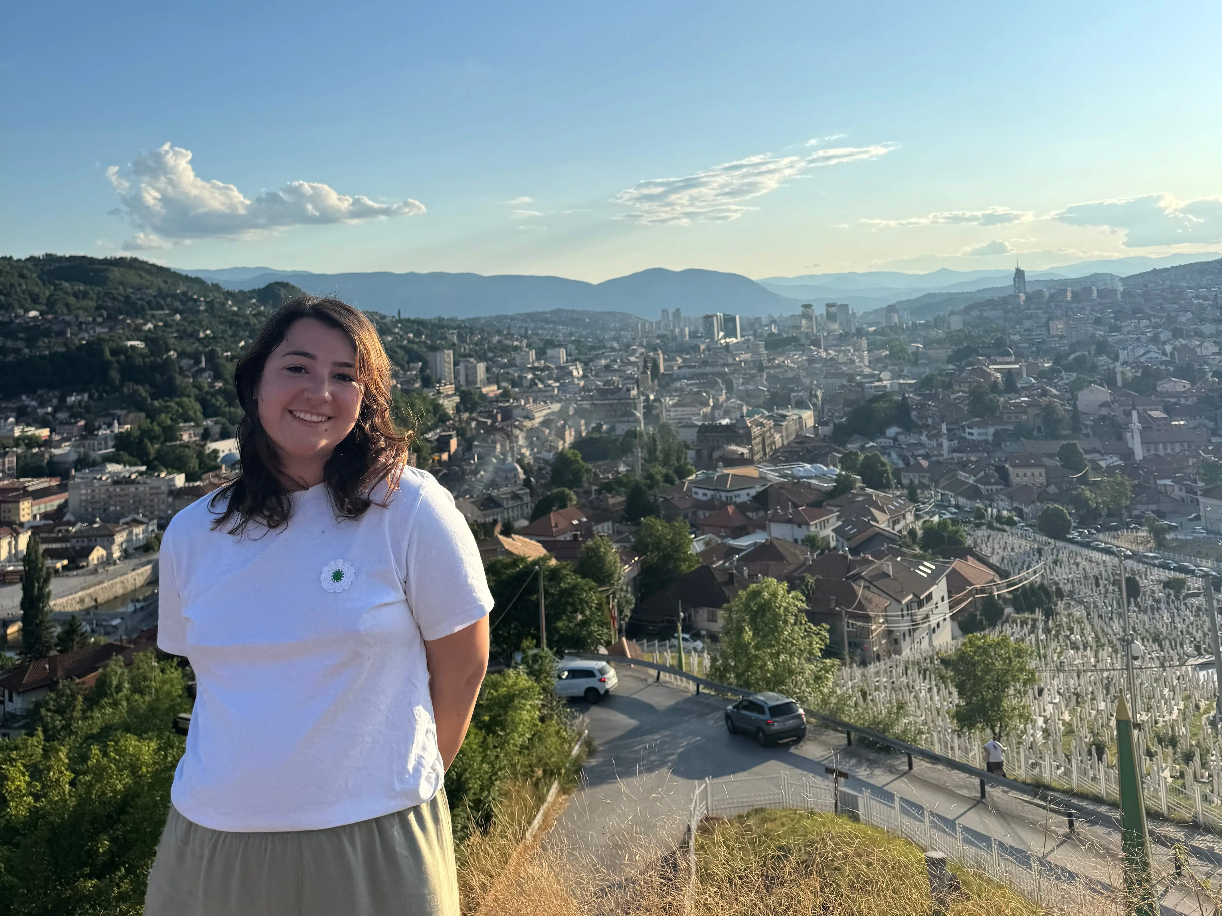 A woman posing with the Yellow Fortress in Sarajevo, Bosnia and Herzegovina, in the background.