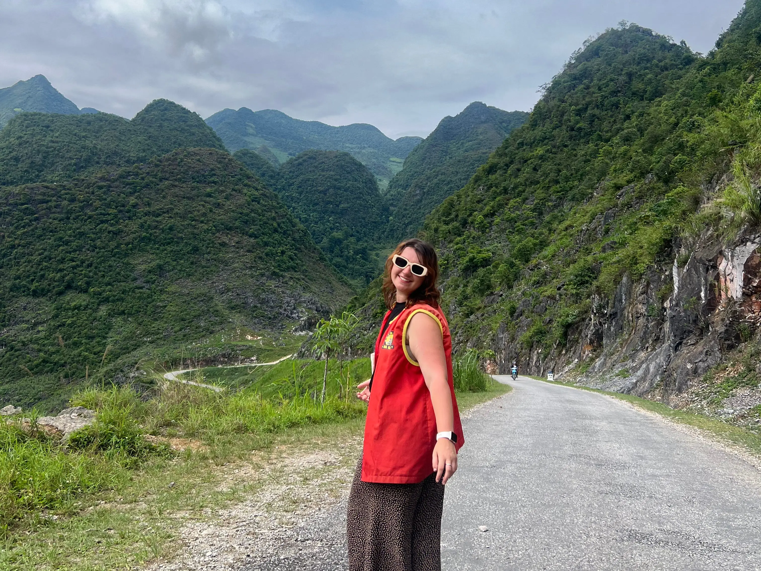 Woman in red, wearing sunglasses, standing on Ha Giang Loop, northern Vietnam.