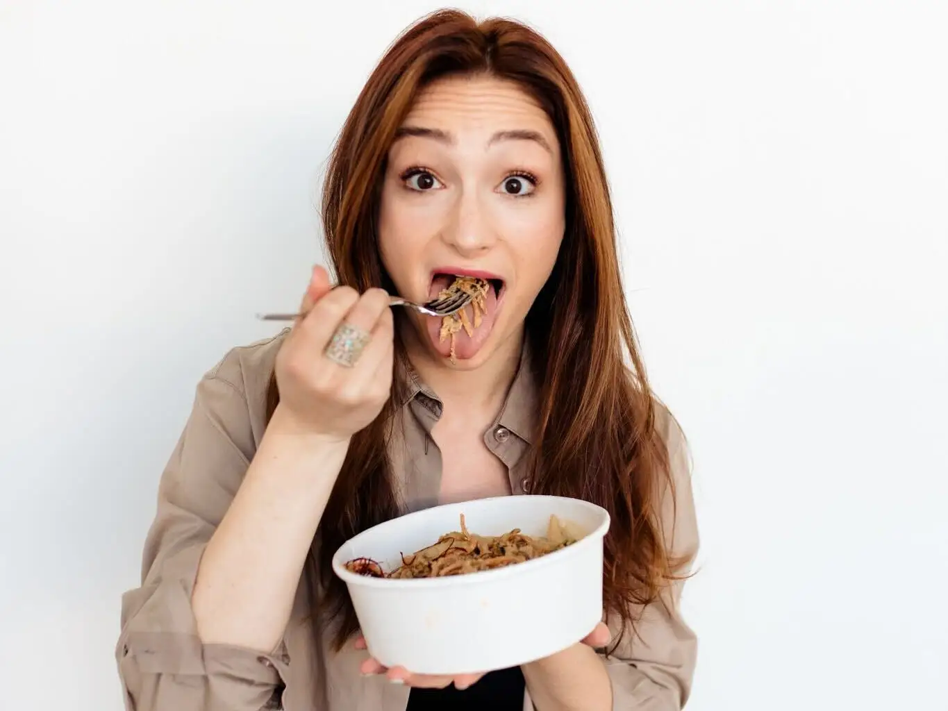 A woman eating a bit from a noodle bowl