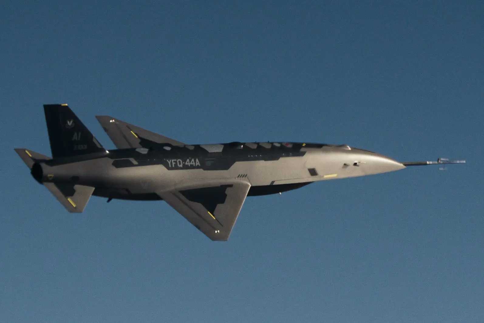A grey and blue aircraft flies against a clear blue sky.