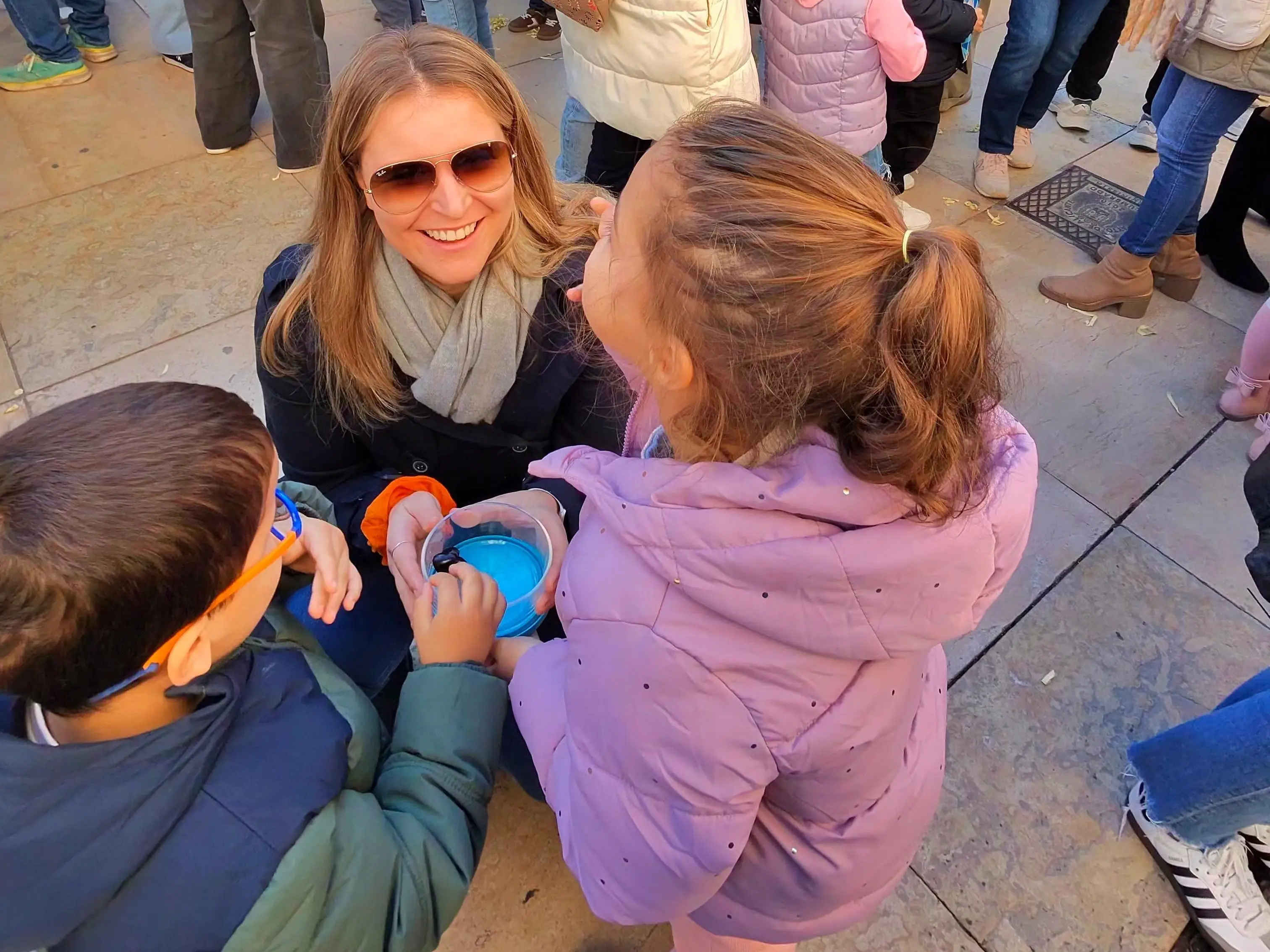 A mother kneeling down to speak with her children in a crowd.