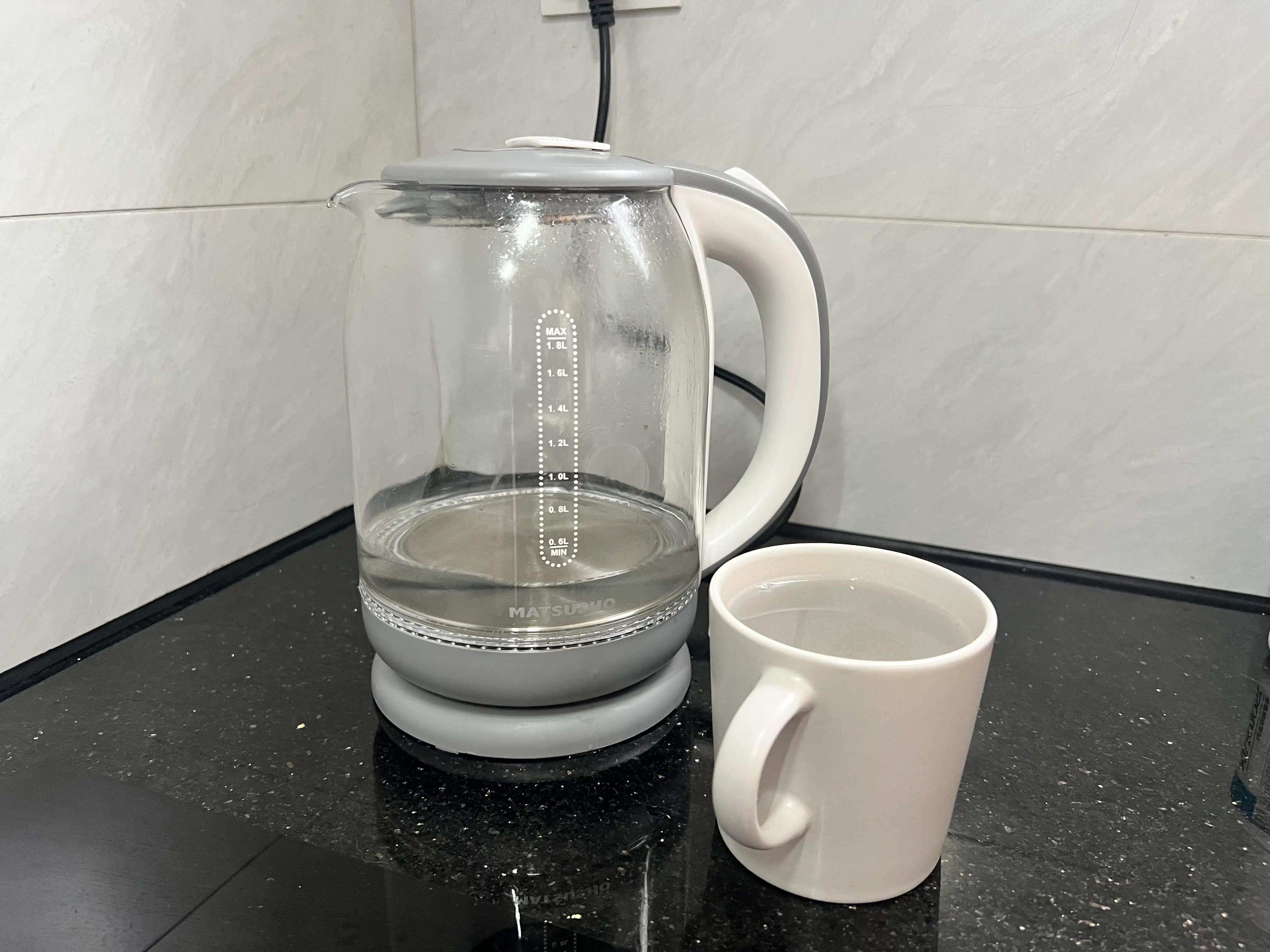 An electric kettle and a white mug with warm water.