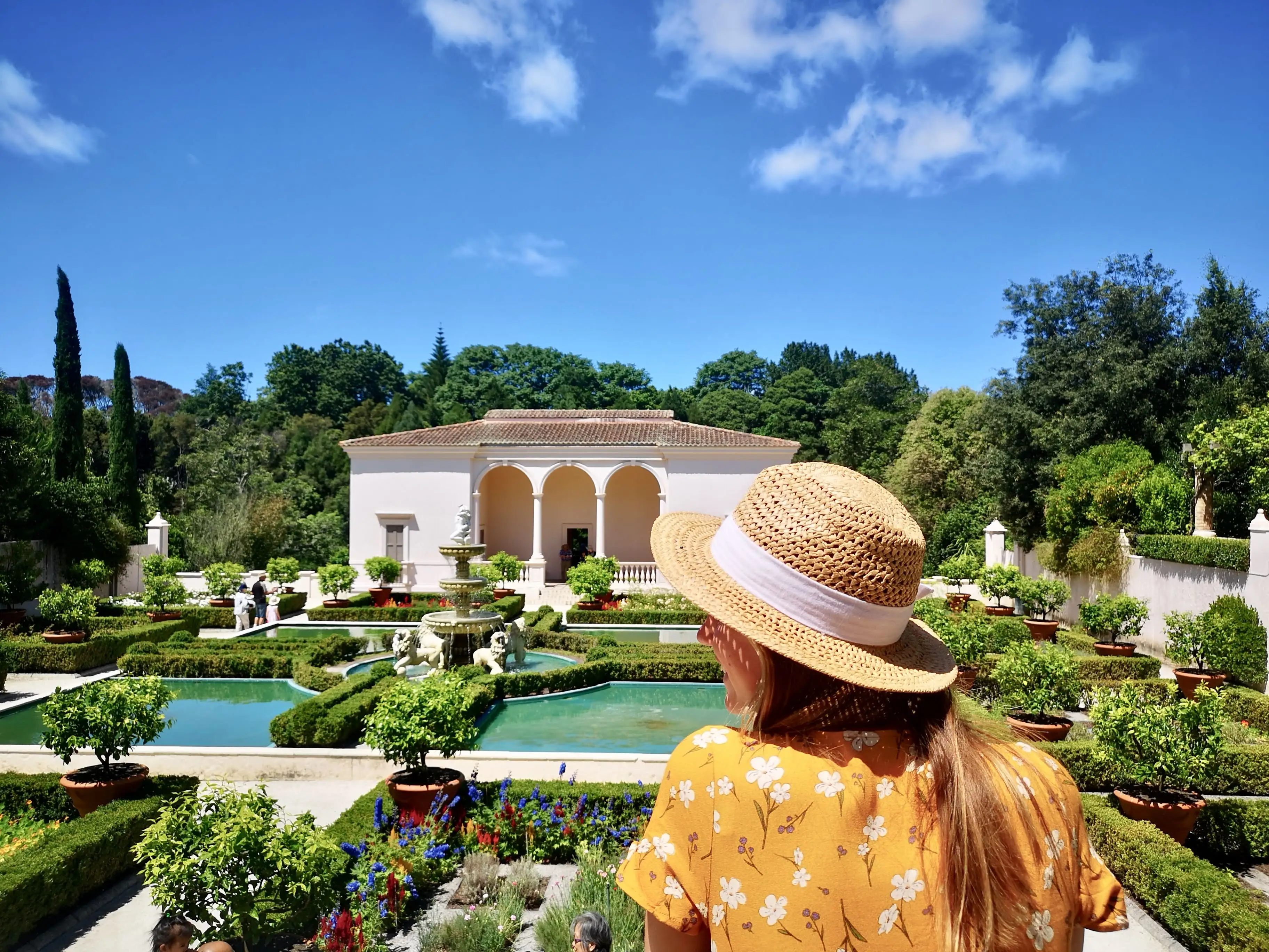 Woman with hat on in front of building surrounded by greenery