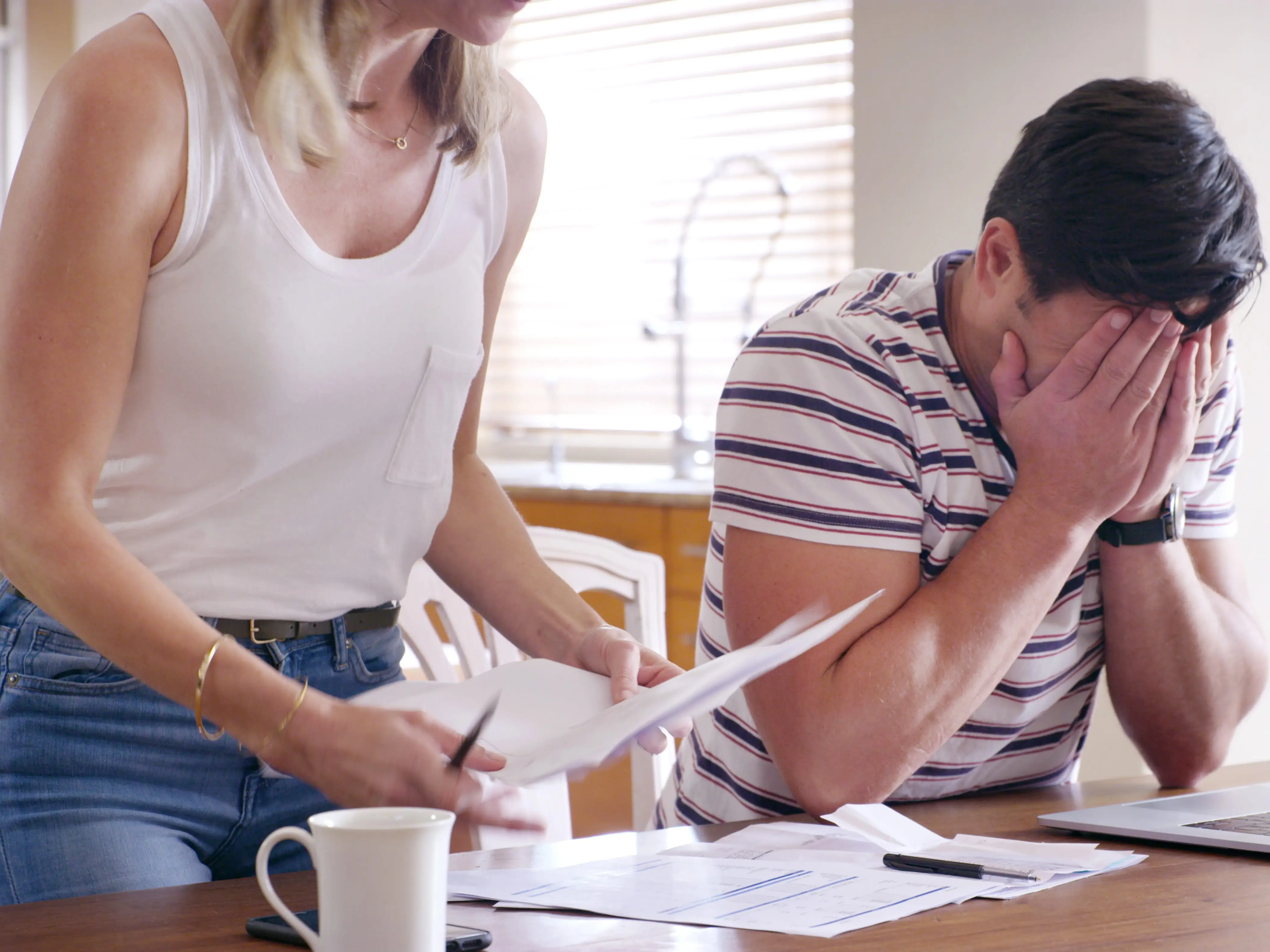 a distraught couple looking at their finances at the kitchen table