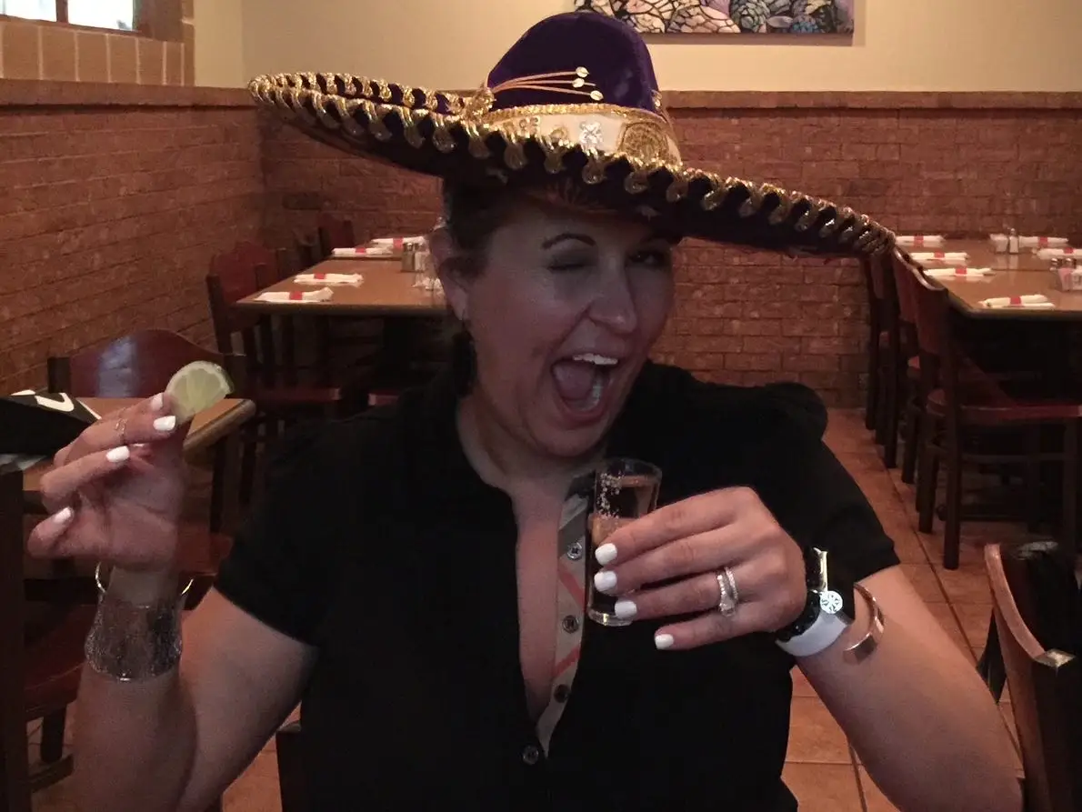 A woman in a sombrero taking a shot of tequila.