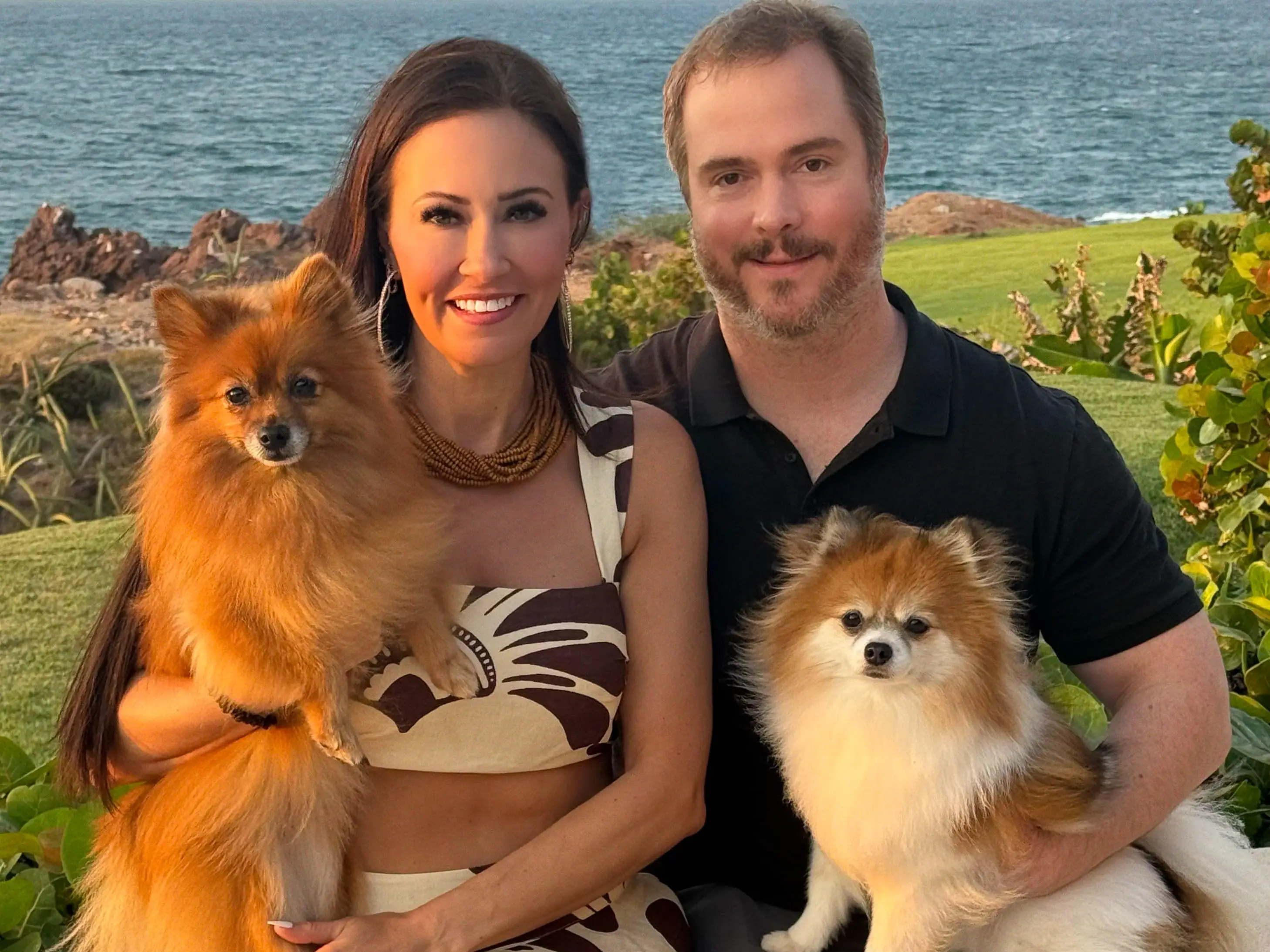 A man and woman holding two dogs in front of the ocean.