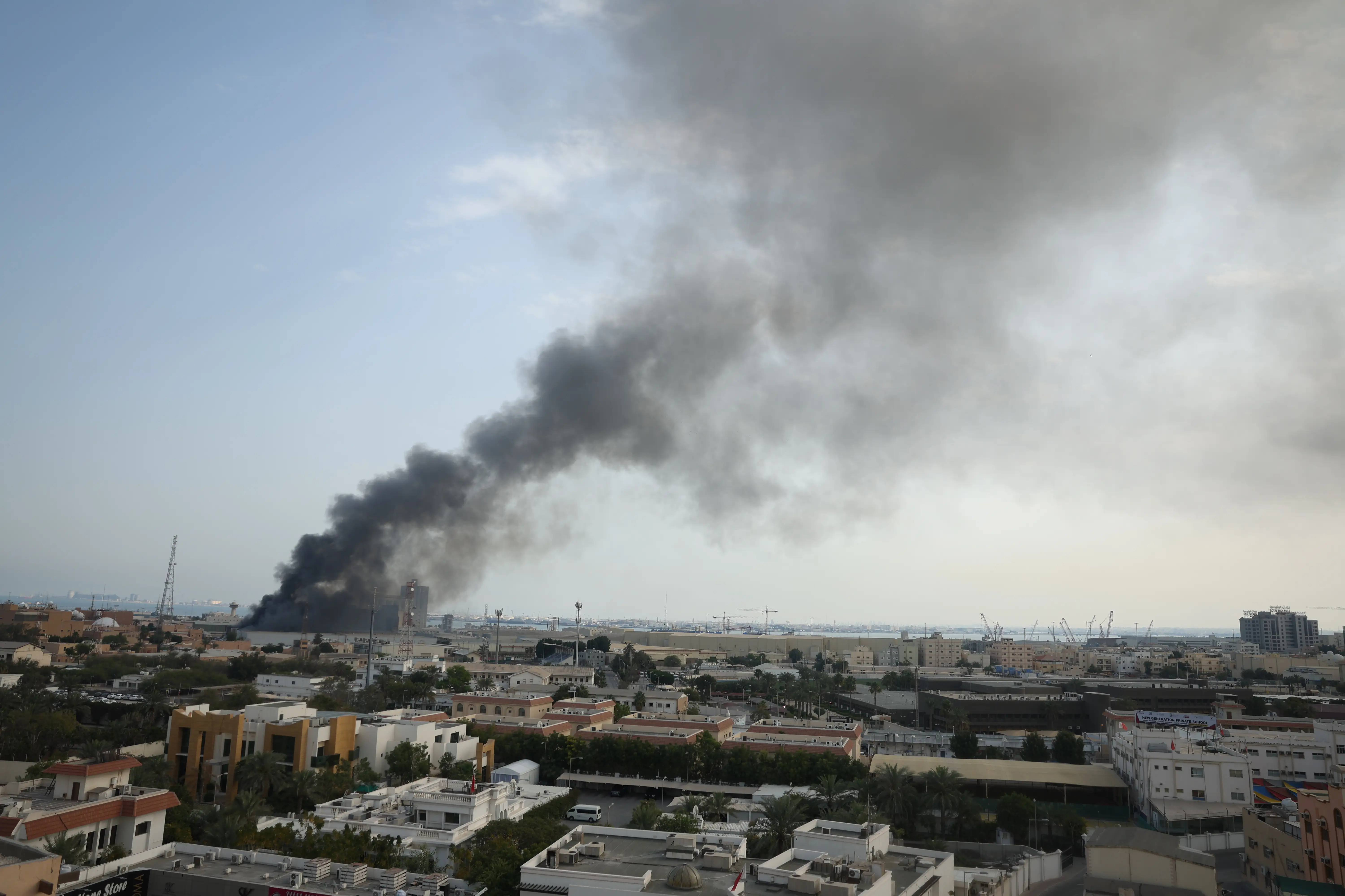 Grey smoke plume in a blue sky over buildings