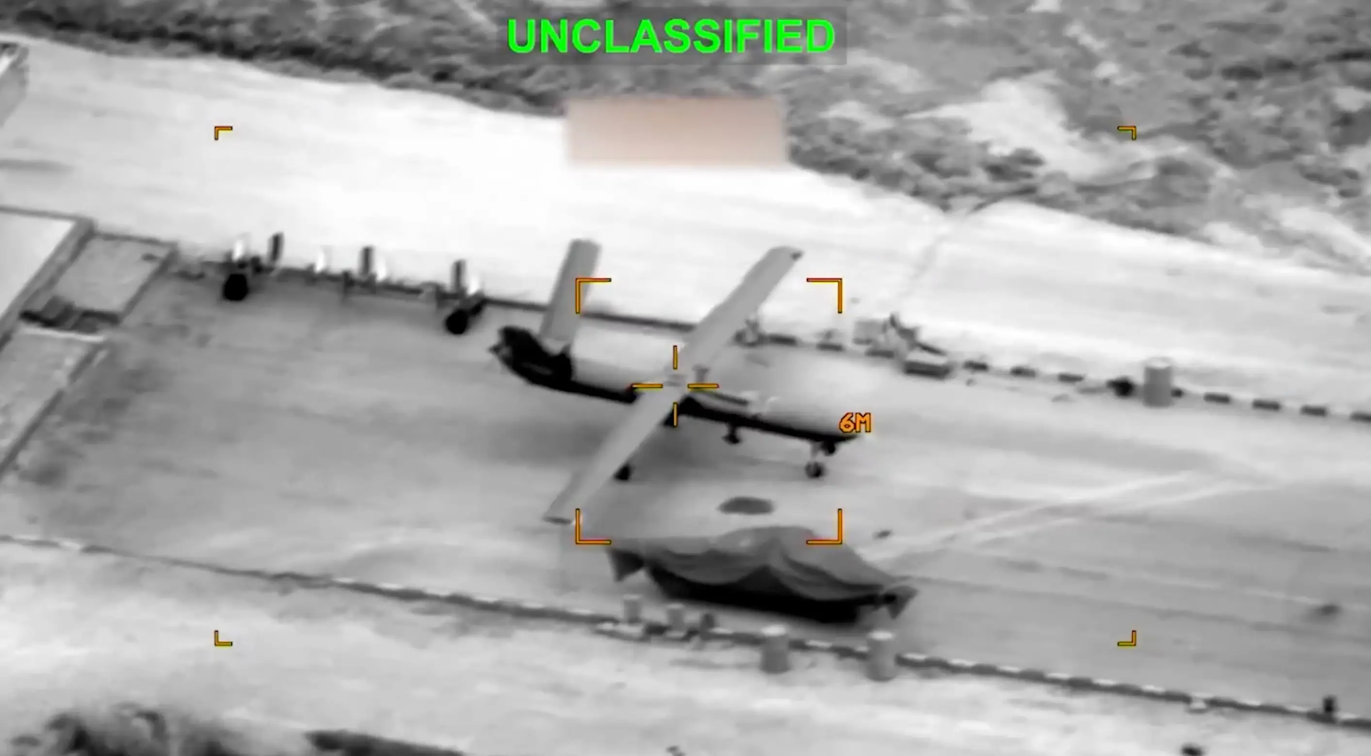 Black and white aerial footage shows a large aircraft on tarmac with the word 'Unclassified' written on the top in large, neon-green letters