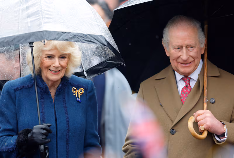 Queen Camilla and King Charles III shelter under umbrellas as they meet members of the public during a walkabout after visiting The Sun Inn on February 5, 2026, in Dedham, Essex.