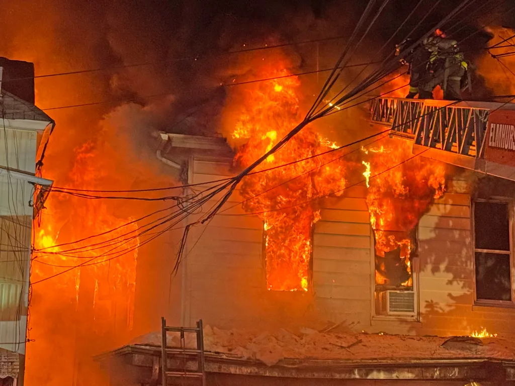A building engulfed in flames with firefighters on a ladder truck.