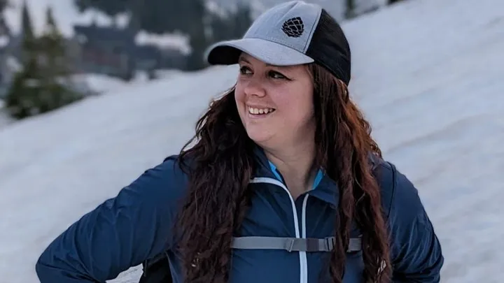 Woman in a gray and black cap and a dark blue jacket in a snowy landscape.