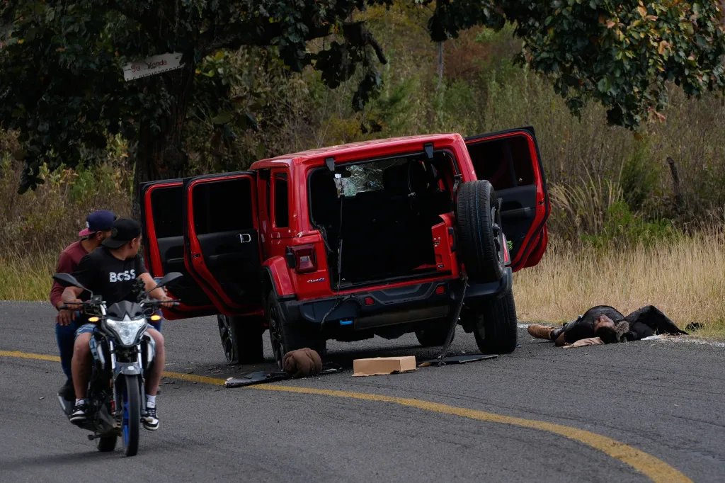 Men ride past a body lying beside a bullet-riddled vehicle in Tapalpa, Mexico, Monday, Feb. 23, 2026, a day after the Mexican army killed Jalisco New Generation Cartel leader Nemesio Oseguera, known as