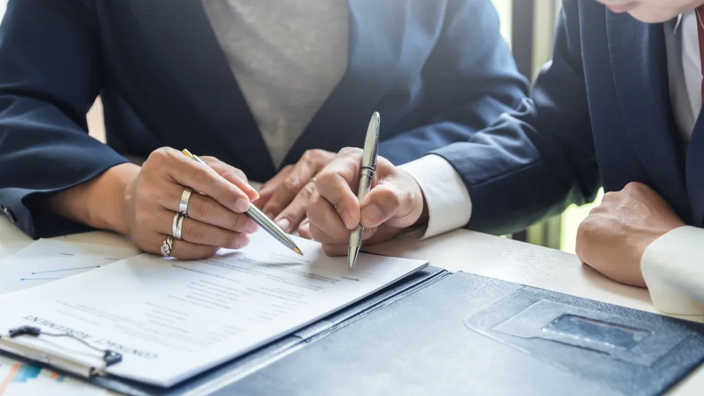 Two people signing a contract at a desk.