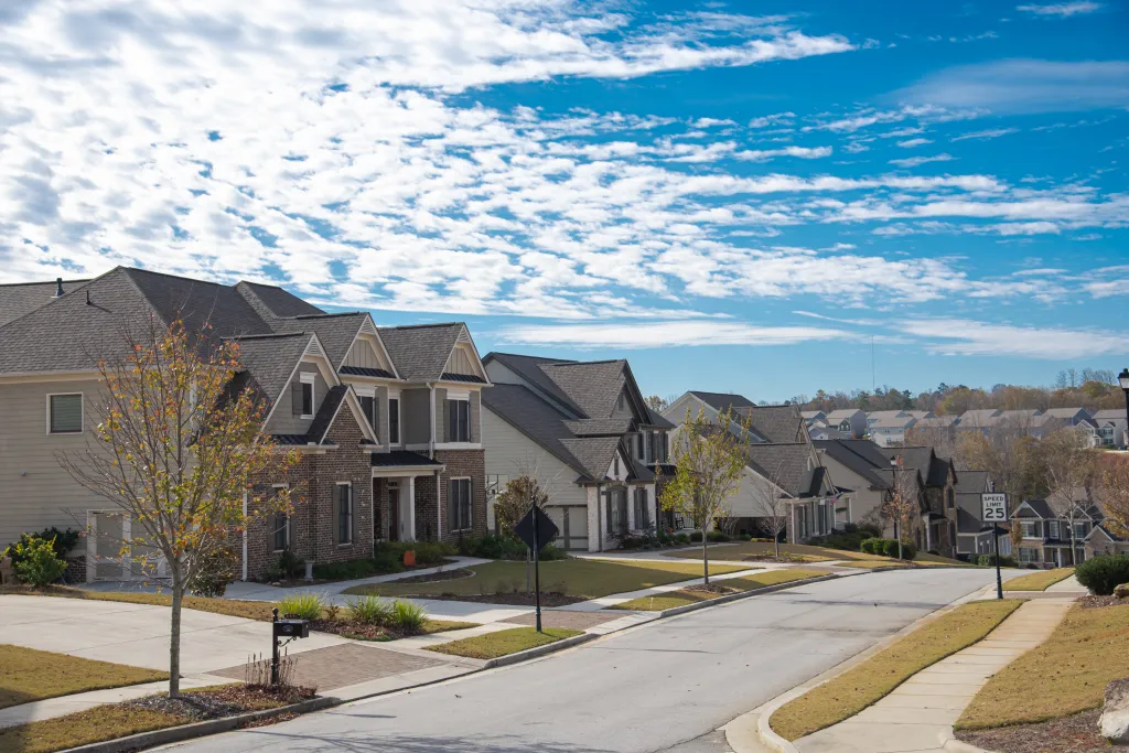 A residential street with a 25 MPH speed limit sign, lined with two-story houses, leads down a steep hill in a new development subdivision in Atlanta, Georgia.
