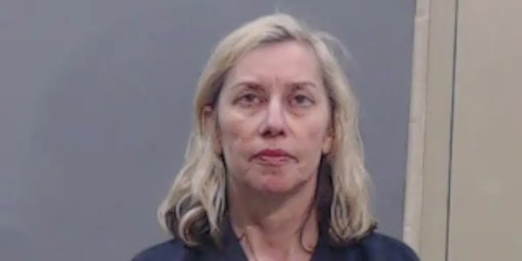 Mugshot of a woman with blonde hair, wearing a dark top, looking forward.