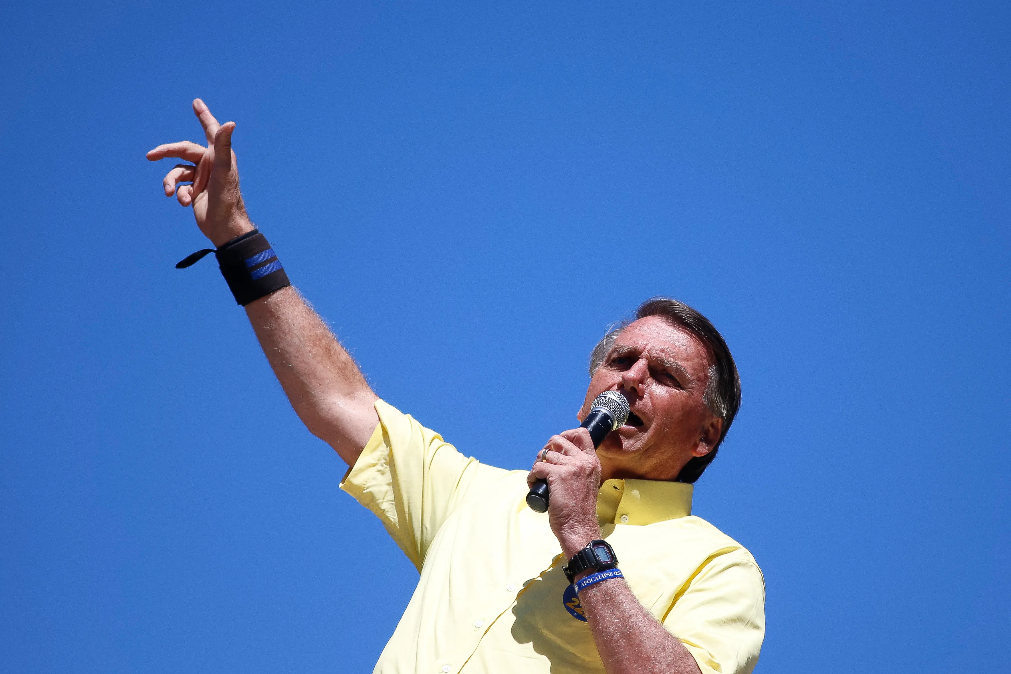 Bolsonaro speaks into a microphone and raises one hand in the sky Bolsonaro speaks into a microphone and raises one hand in the sky