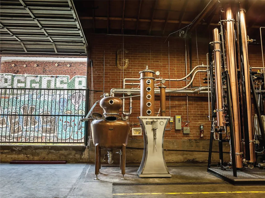 Interior of Greenbar Distillery in Los Angeles, showing distillation equipment and a view of graffiti outside.